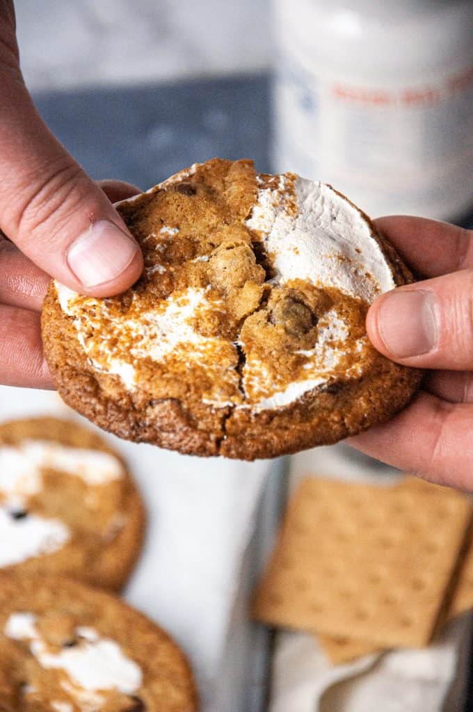 Hands breaking open a s'mores chocolate chip cookie to show chewy interior texture