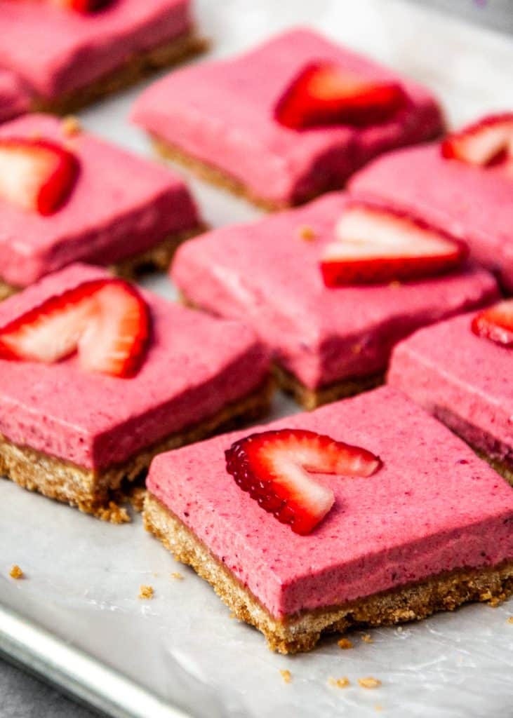 Cut strawberry dessert bars on a sheet tray. Each square is topped with a strawberry slice. 