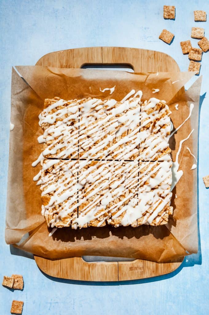 cinnamon toast crunch milk and cereal treats sliced into bars, drizzled with milk icing, on a cutting board layered with parchment paper