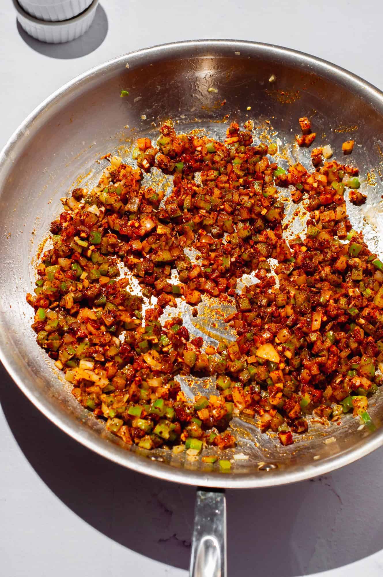 Diced celery, onion, green bell pepper in a pan with red Cajun seasoning