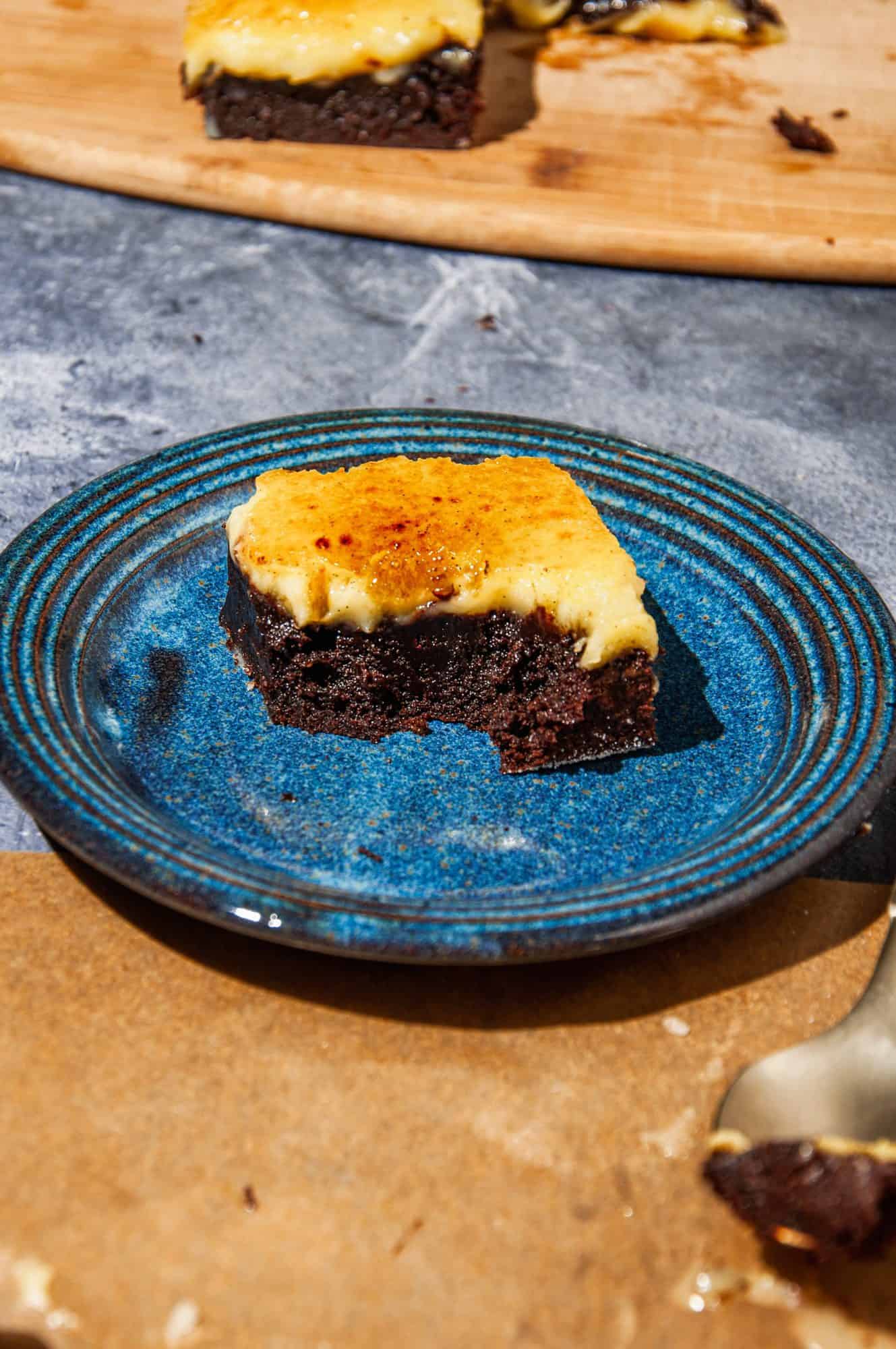 Brownie with creme brûlée top layer with golden crust on a blue plate, with a bite taken out of it.