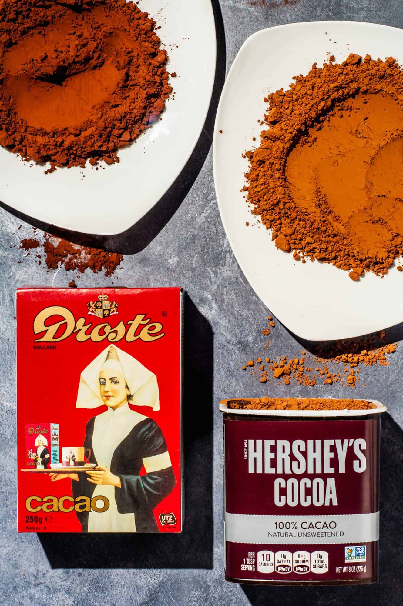 Droste cocoa powder packaging and Hershey's cocoa powder packaging with cocoa powder on white plates above packaging to show color difference. 