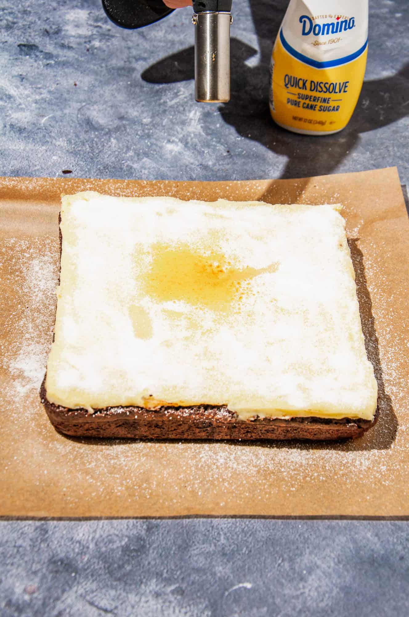 Creme brulee brownies covered in a thin layer of superfine sugar, beginning to turn golden from torch