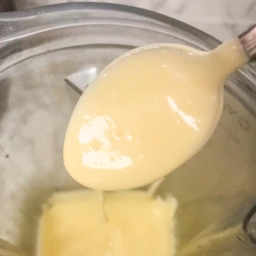 close up of hollandaise sauce on a spoon over blender