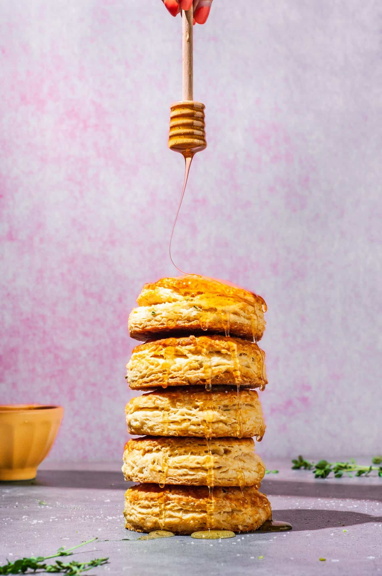 drizzling honey over a stack of 5 flaky biscuits with thyme