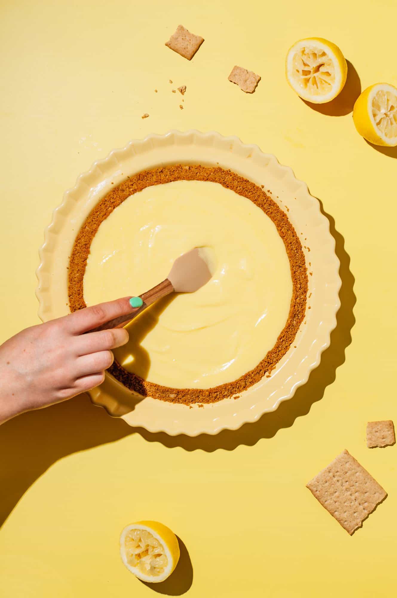 hand with spatula spreading lemon curd into cooked graham cracker pie crust