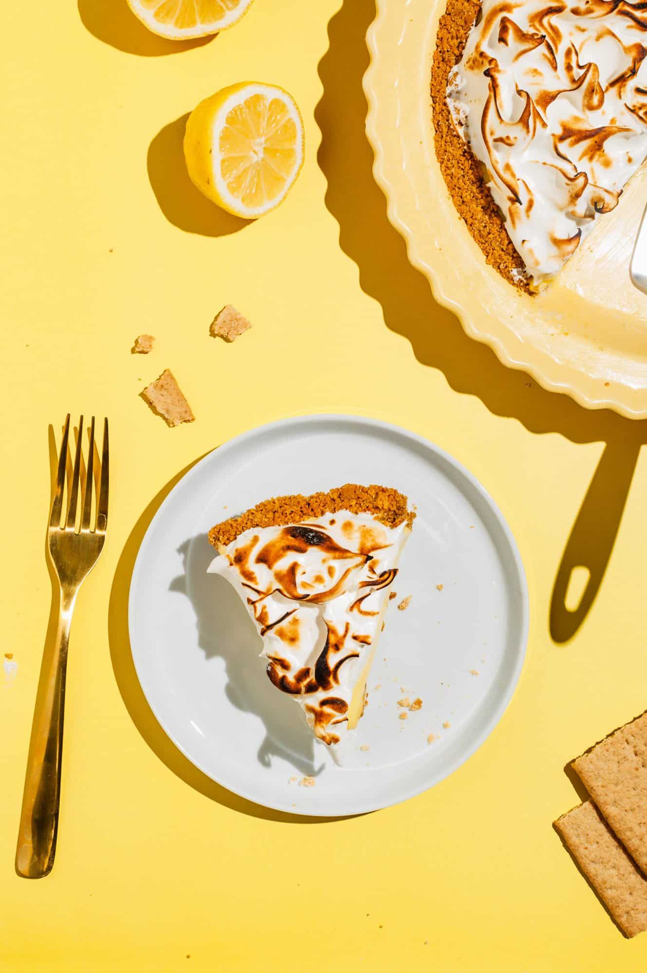 a slice of lemon meringue pie on a white plate with graham cracker crumbs