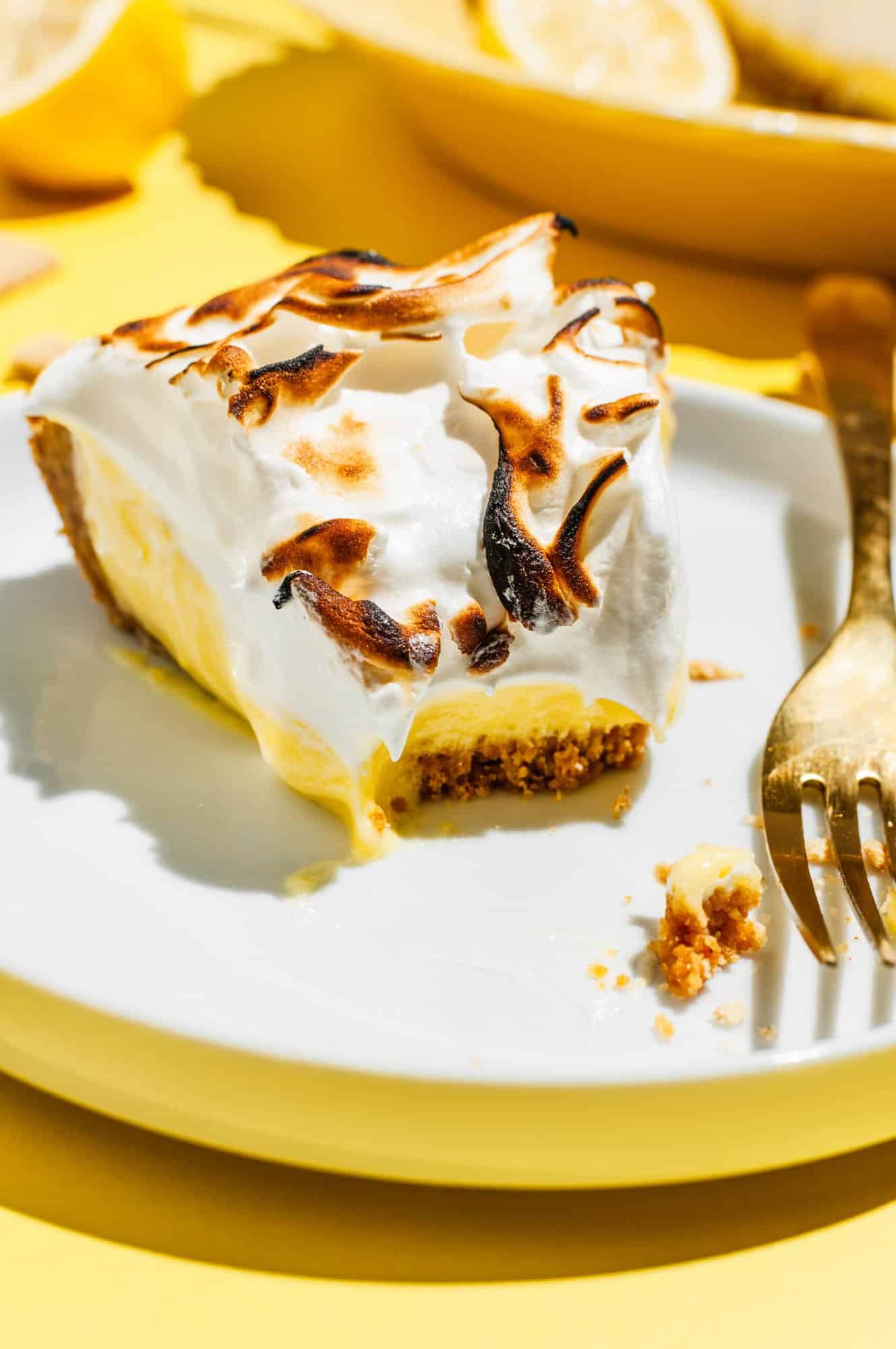 slice of lemon meringue pie on a plate with a bite taken out with a fork to the side