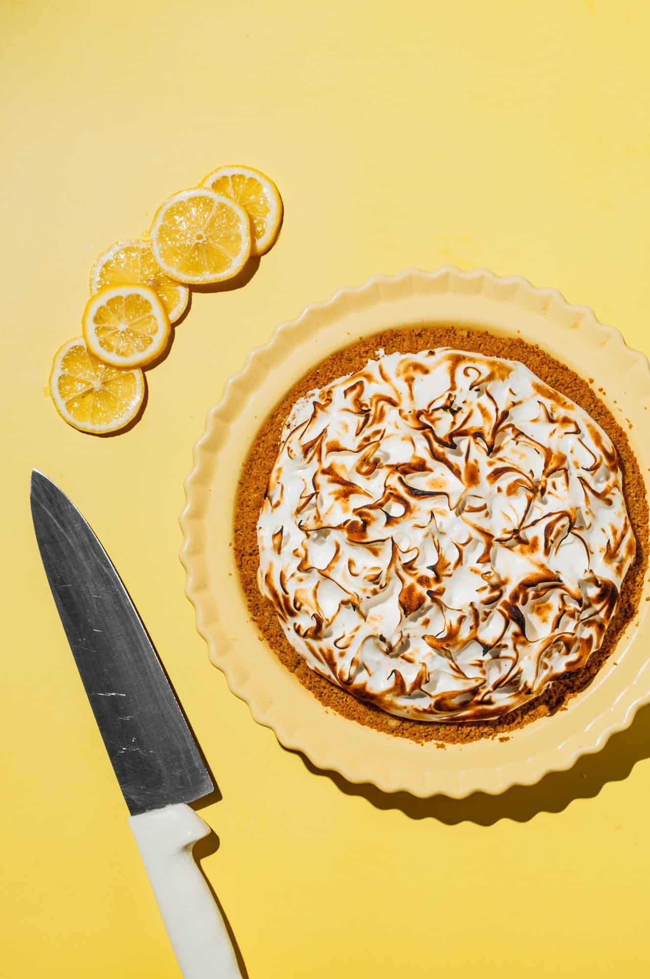 lemon meringue pie in yellow pie plate with lemon slices and a knife to the side