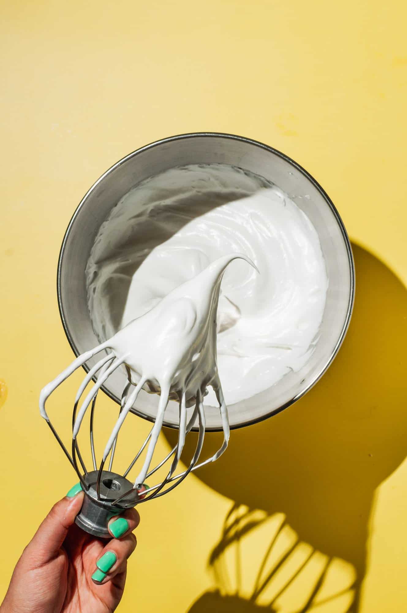 hand holding whisk over a bowl of Swiss meringue 