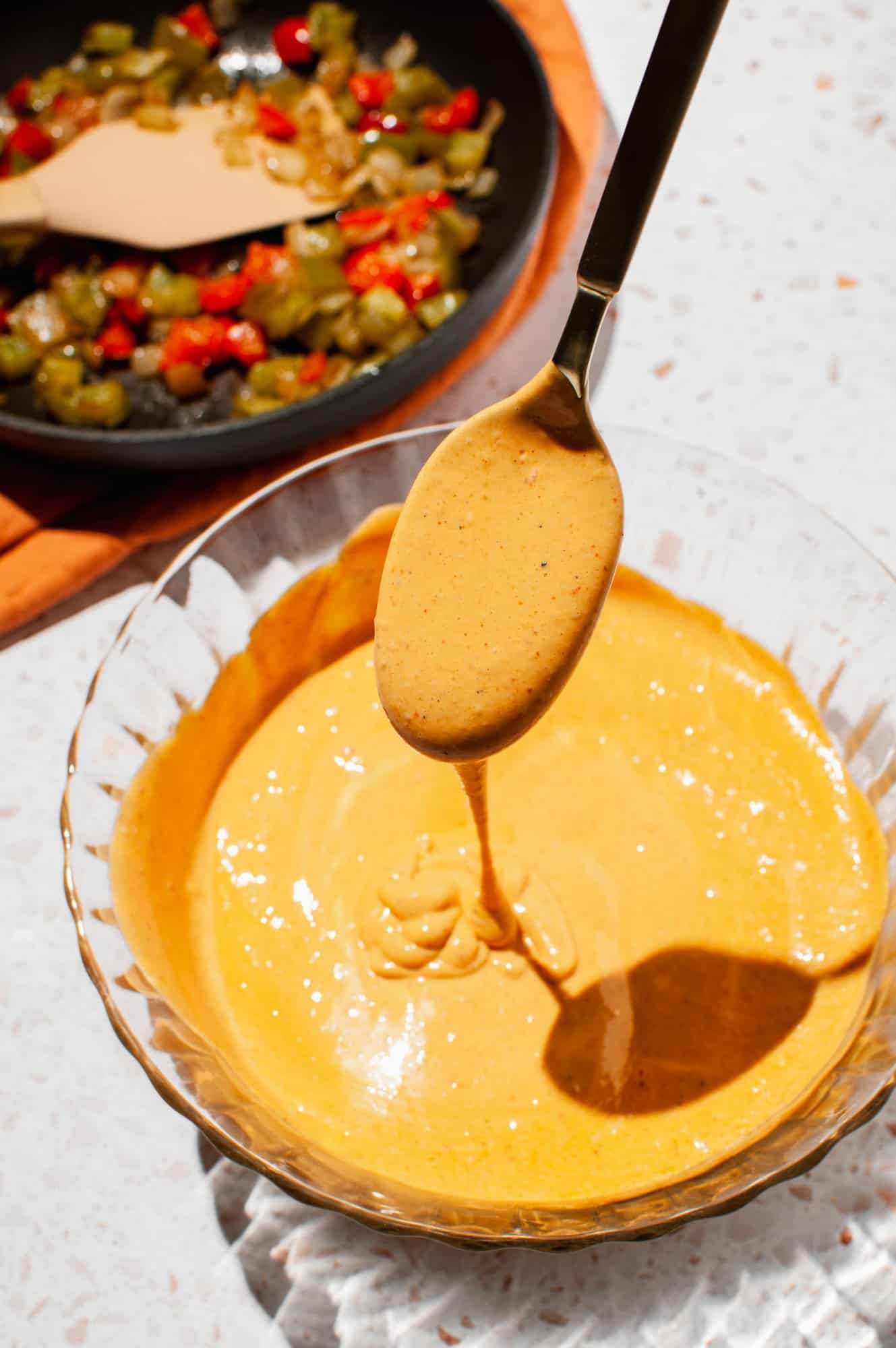 close up of chipotle hollandaise sauce dripping off of a spoon into bowl with sauce