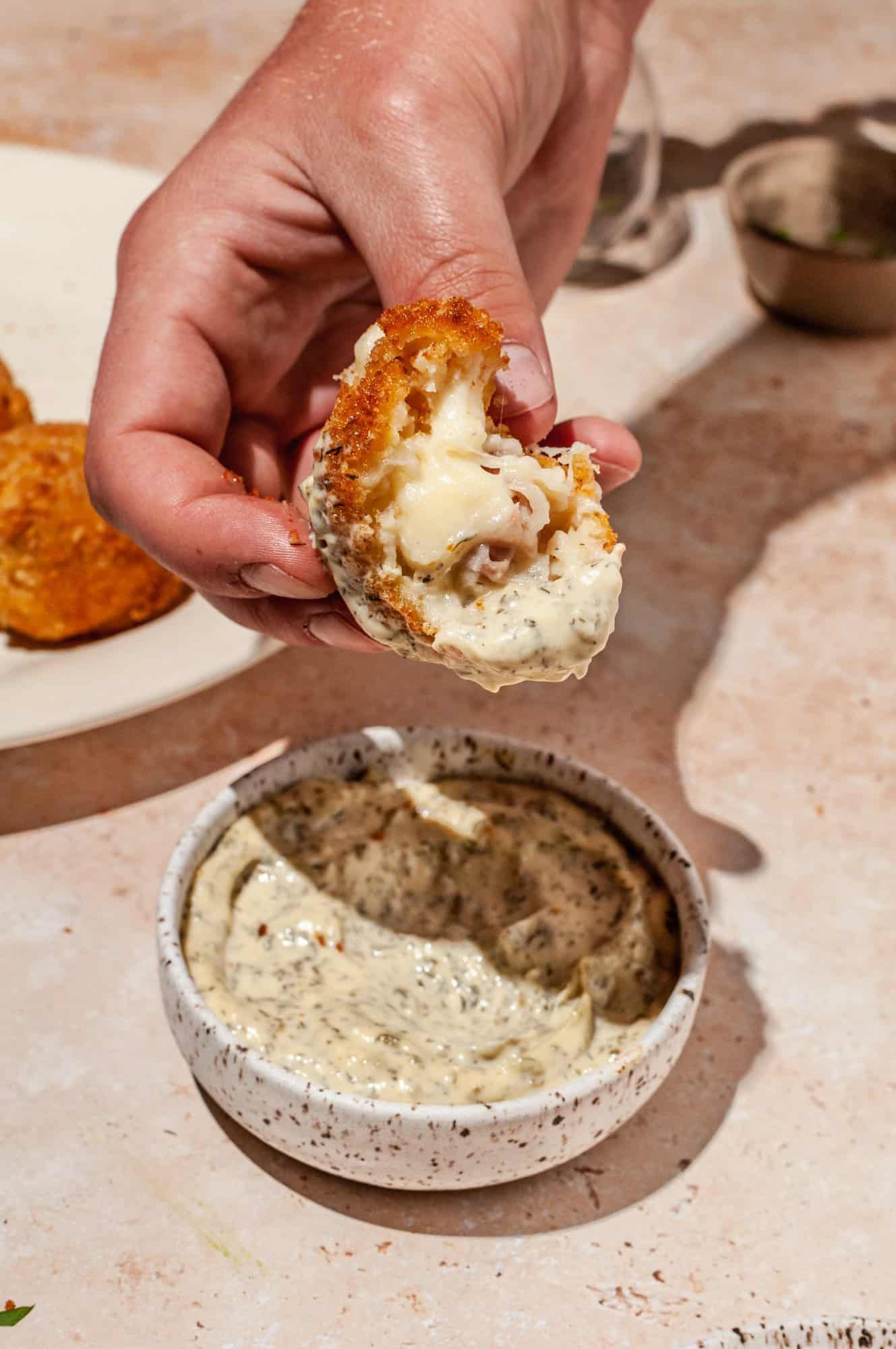dipping half ham croquette into aioli, showing melted cheese on inside