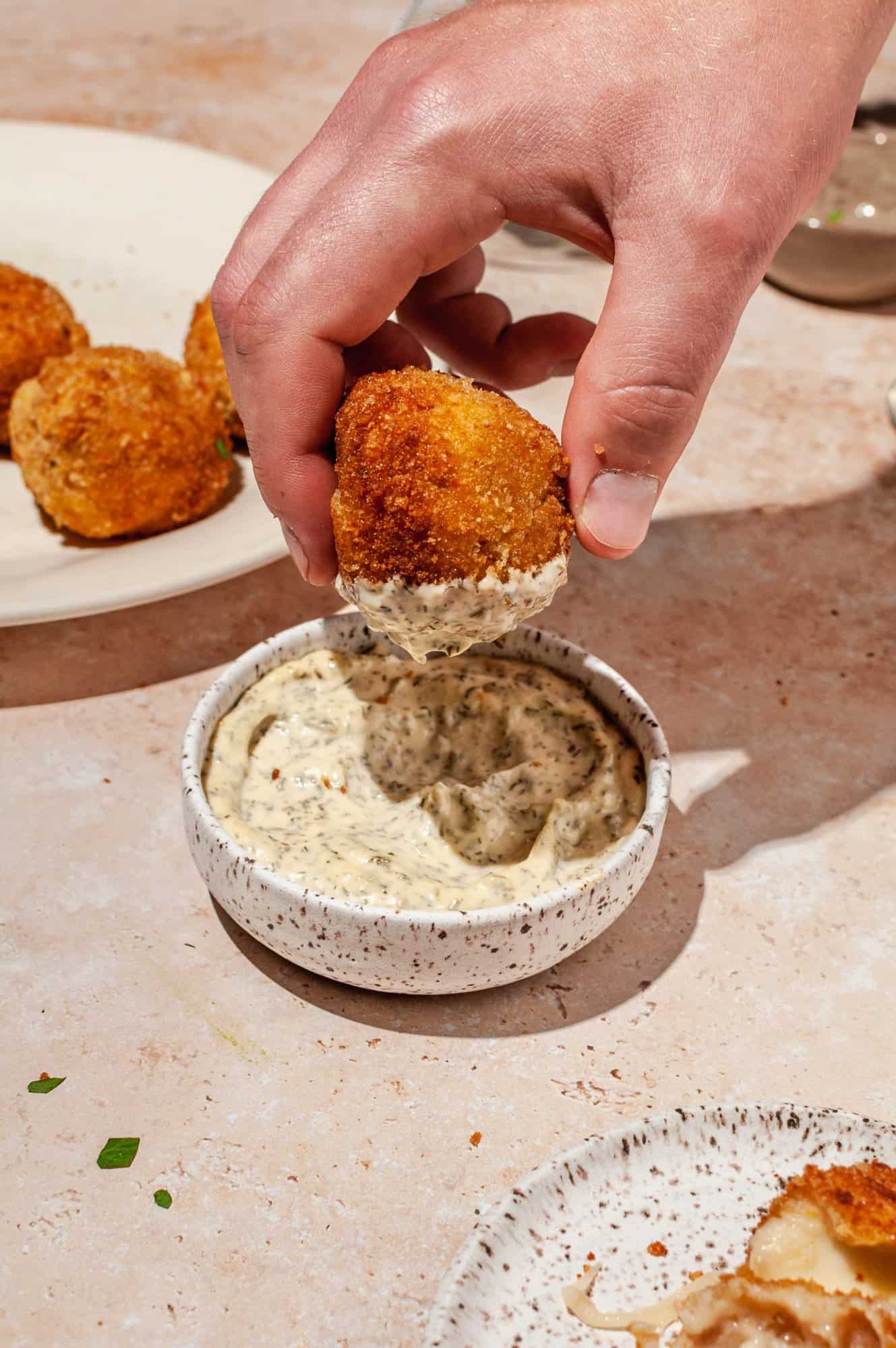 hand dipping ham and cheese croquette into bowl of aioli