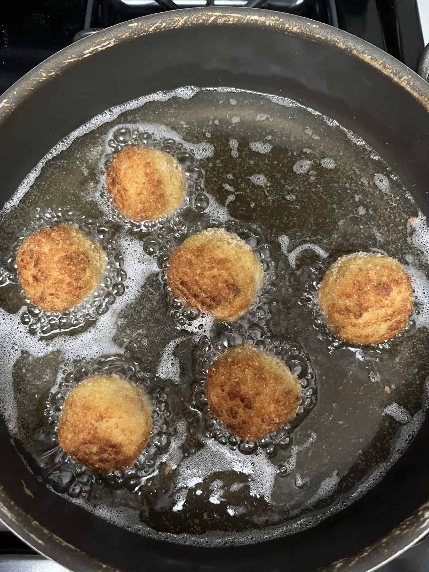 six croquettes frying in oil after flipping