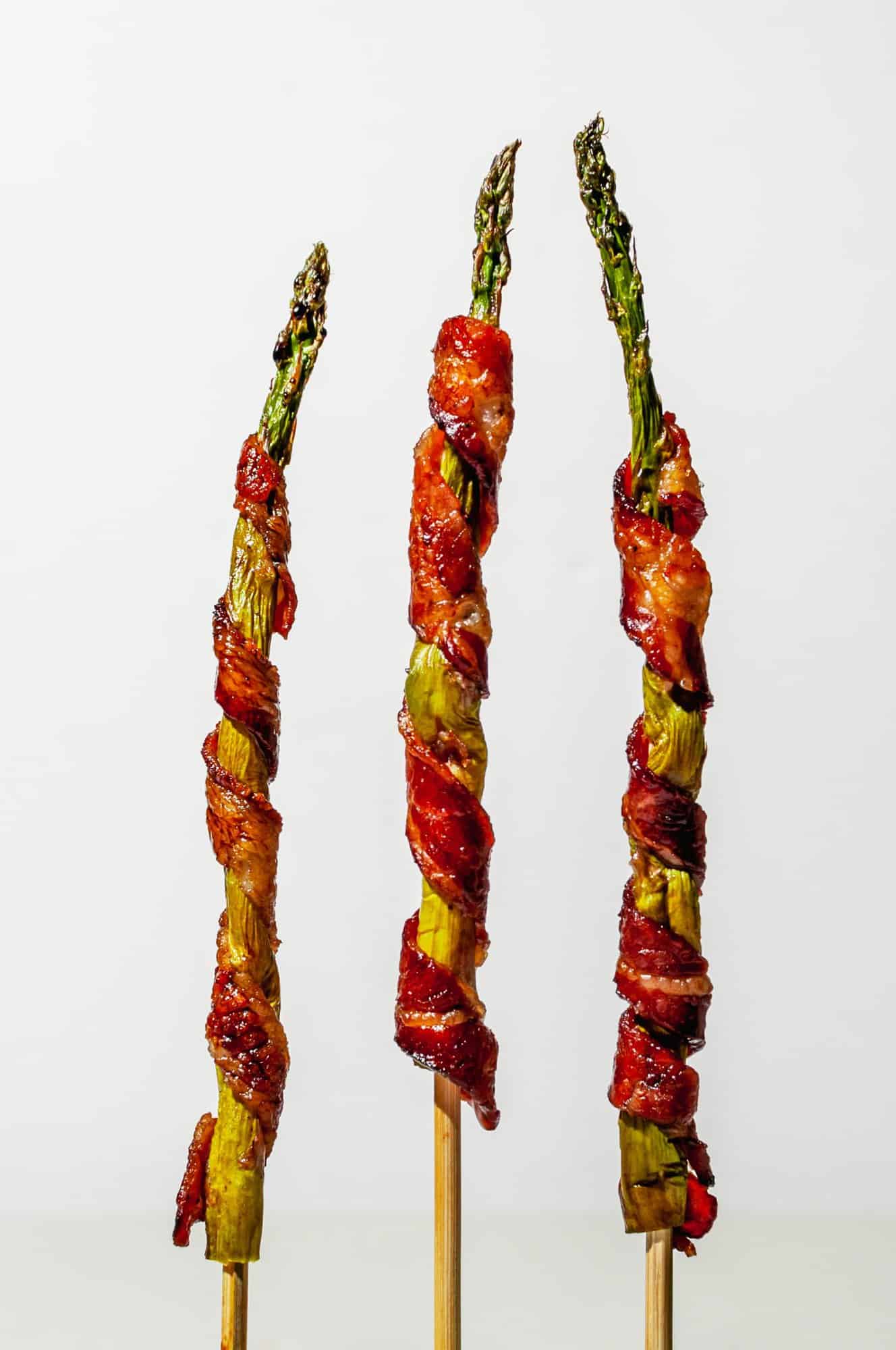 3 asparagus spears wrapped in bacon standing straight up on skewers