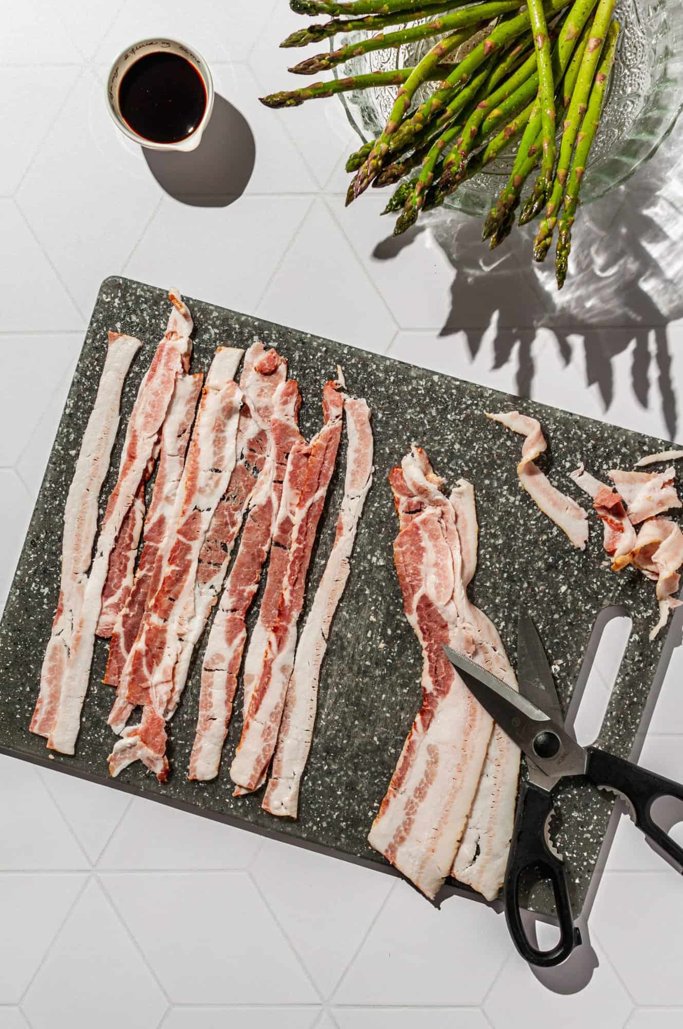 cutting bacon into long thin strips with kitchen shears on a cutting board