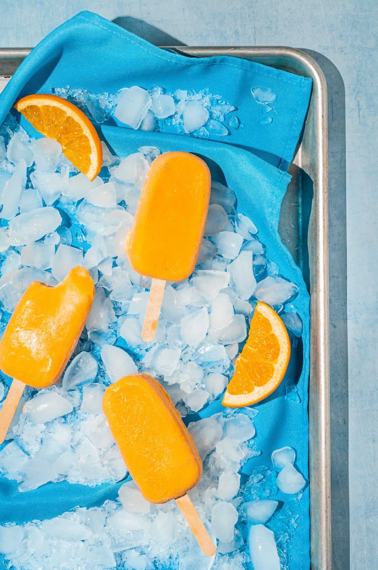 three orange popsicles on blue linen with crushed ice