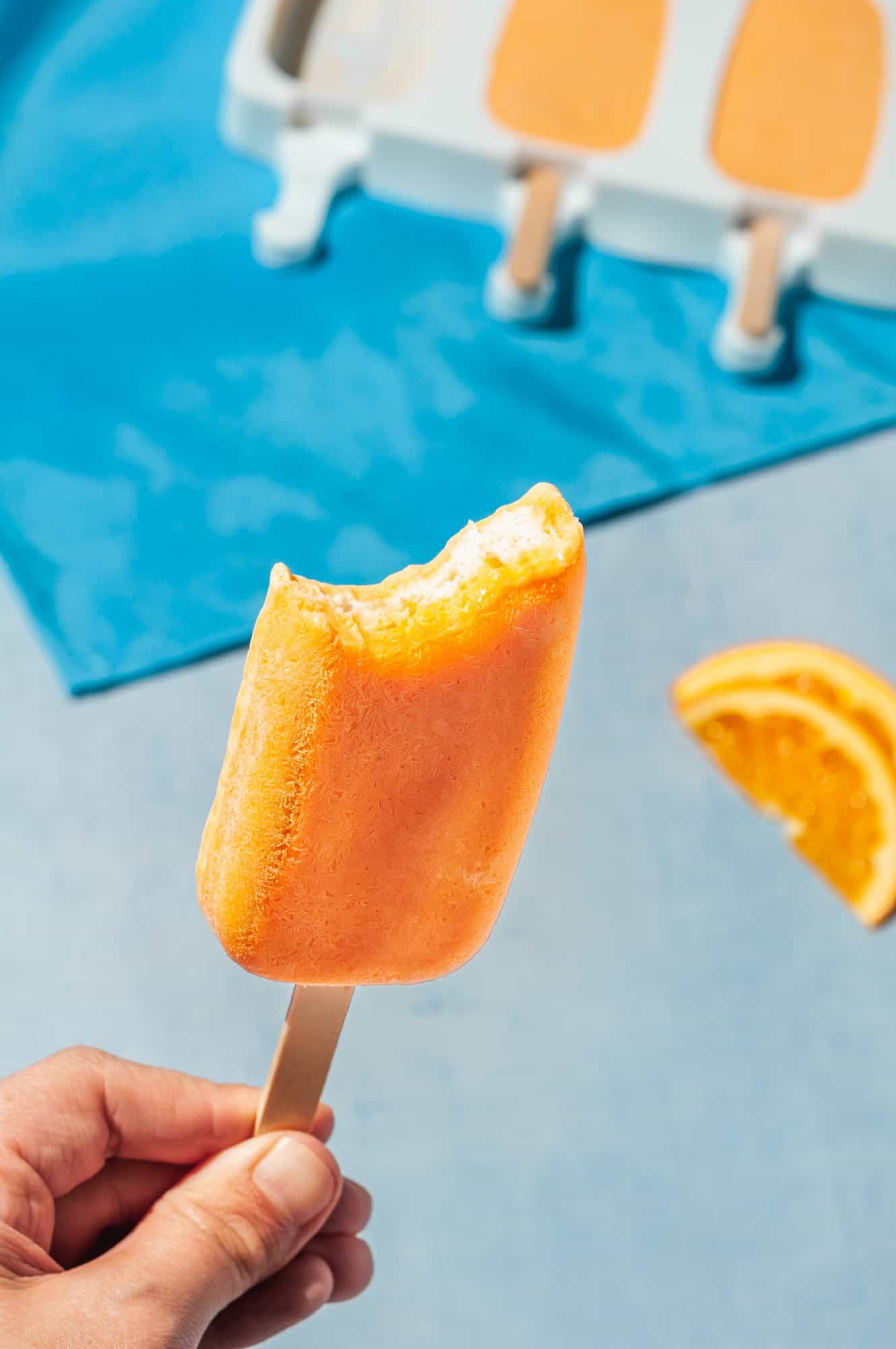 hand holding an orange creamsicle popsicle with bite out of it