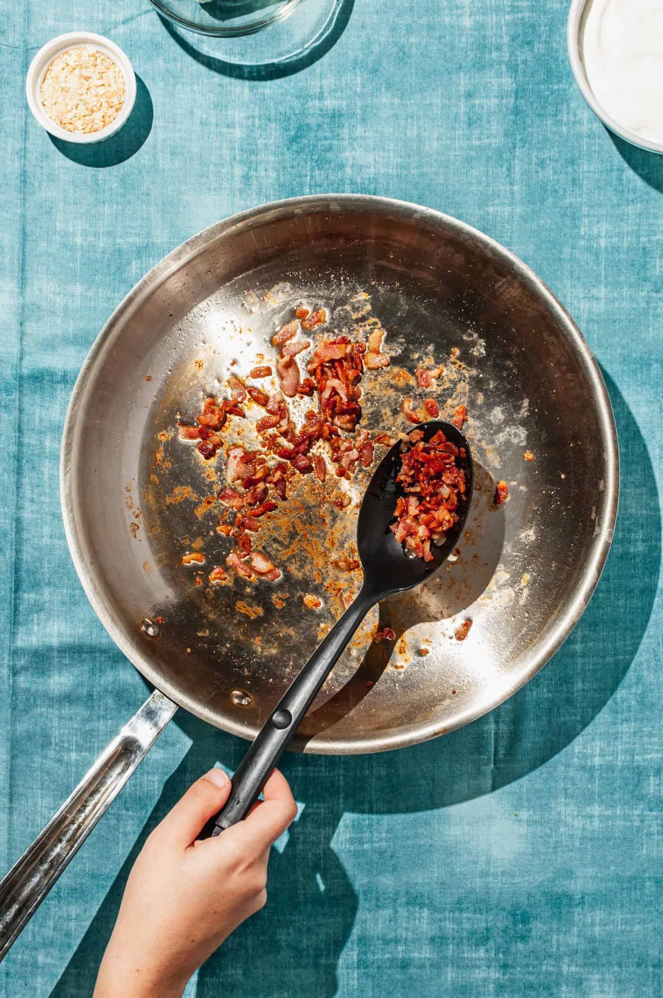 removing crispy bacon bits from skillet with slotted spoon
