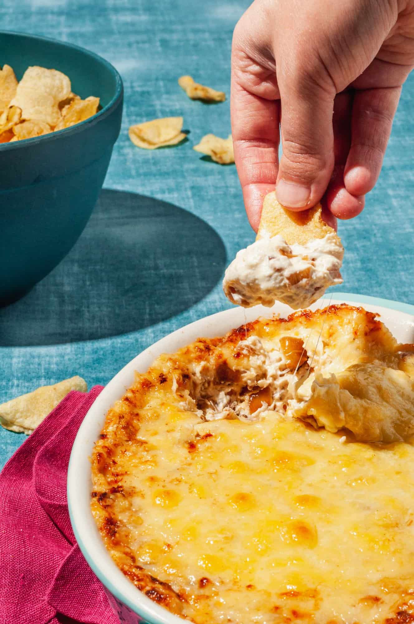 hand dipping chip into caramelized onion dip, bowl of chips to the side