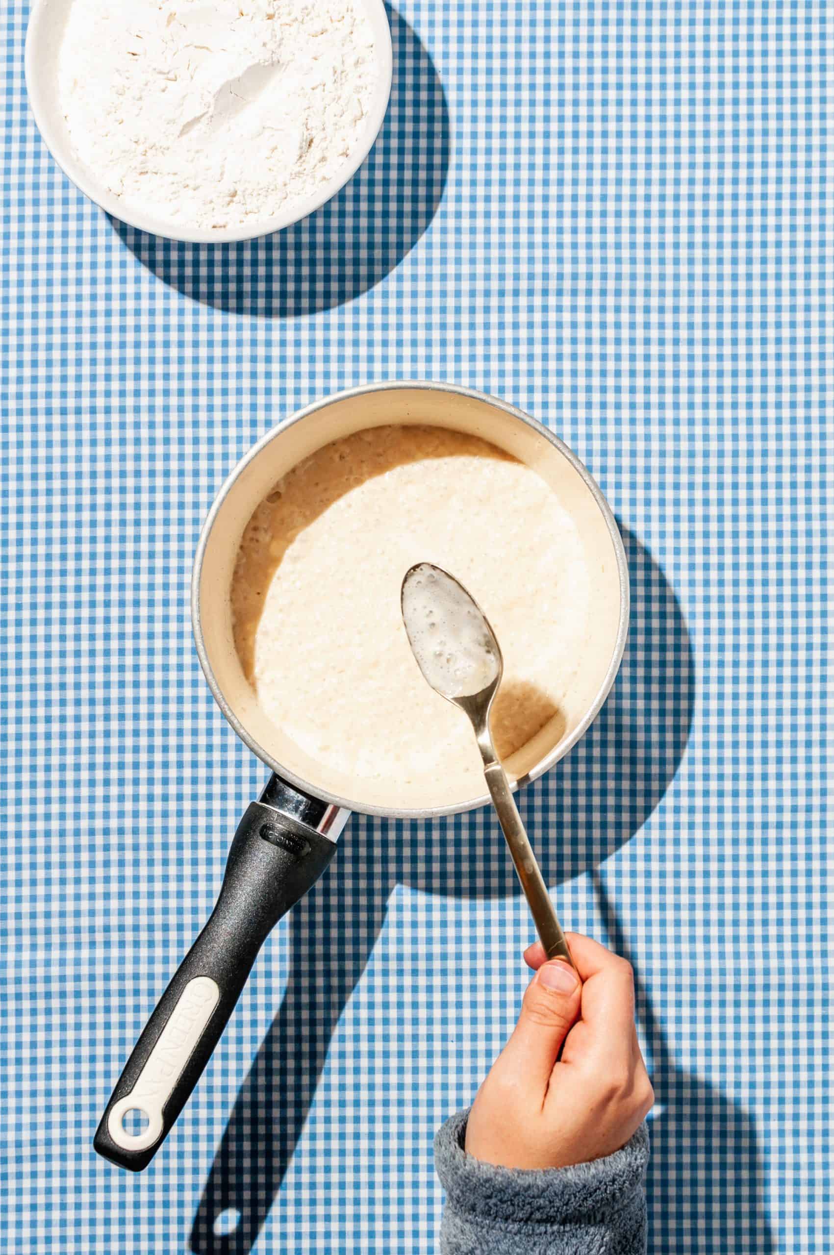 hand holding spoon with foamy yeast mixture over sauce pot