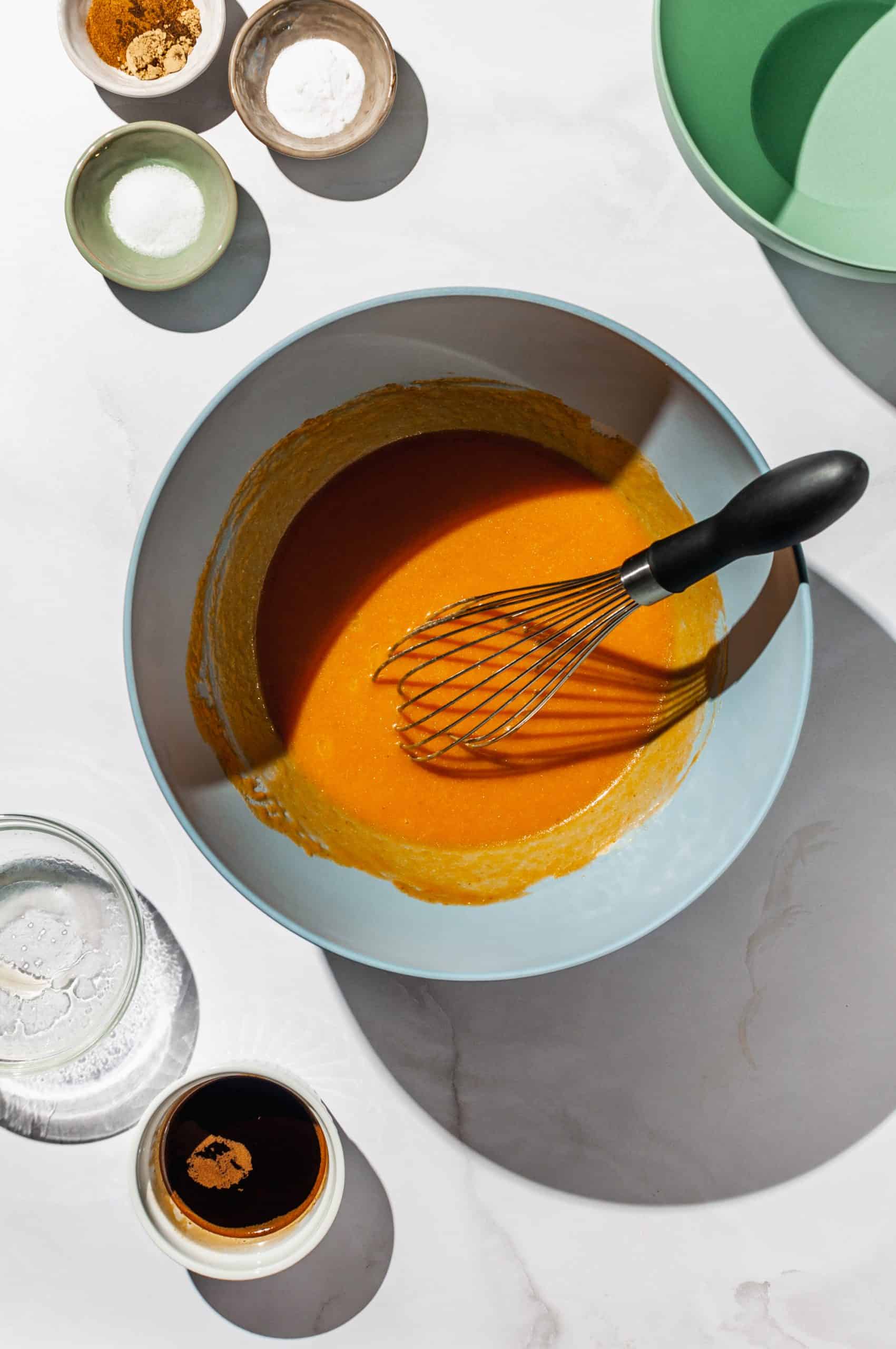 smooth pumpkin puree mixture in mixing bowl with whisk, extra ingredients on the side