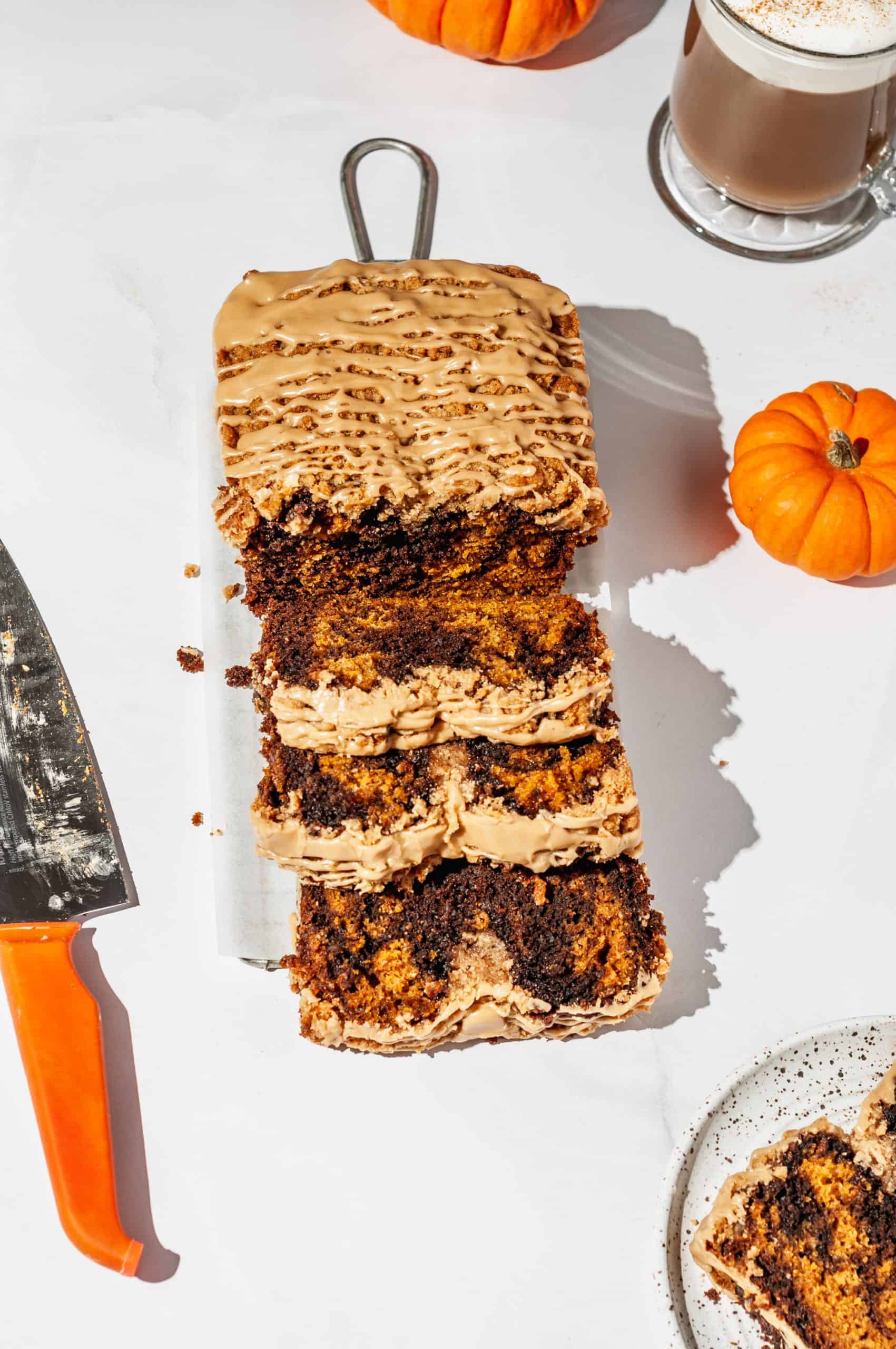 sliced streusel loaf showing marbled brown and orange inside, pumpkin spice latte in back