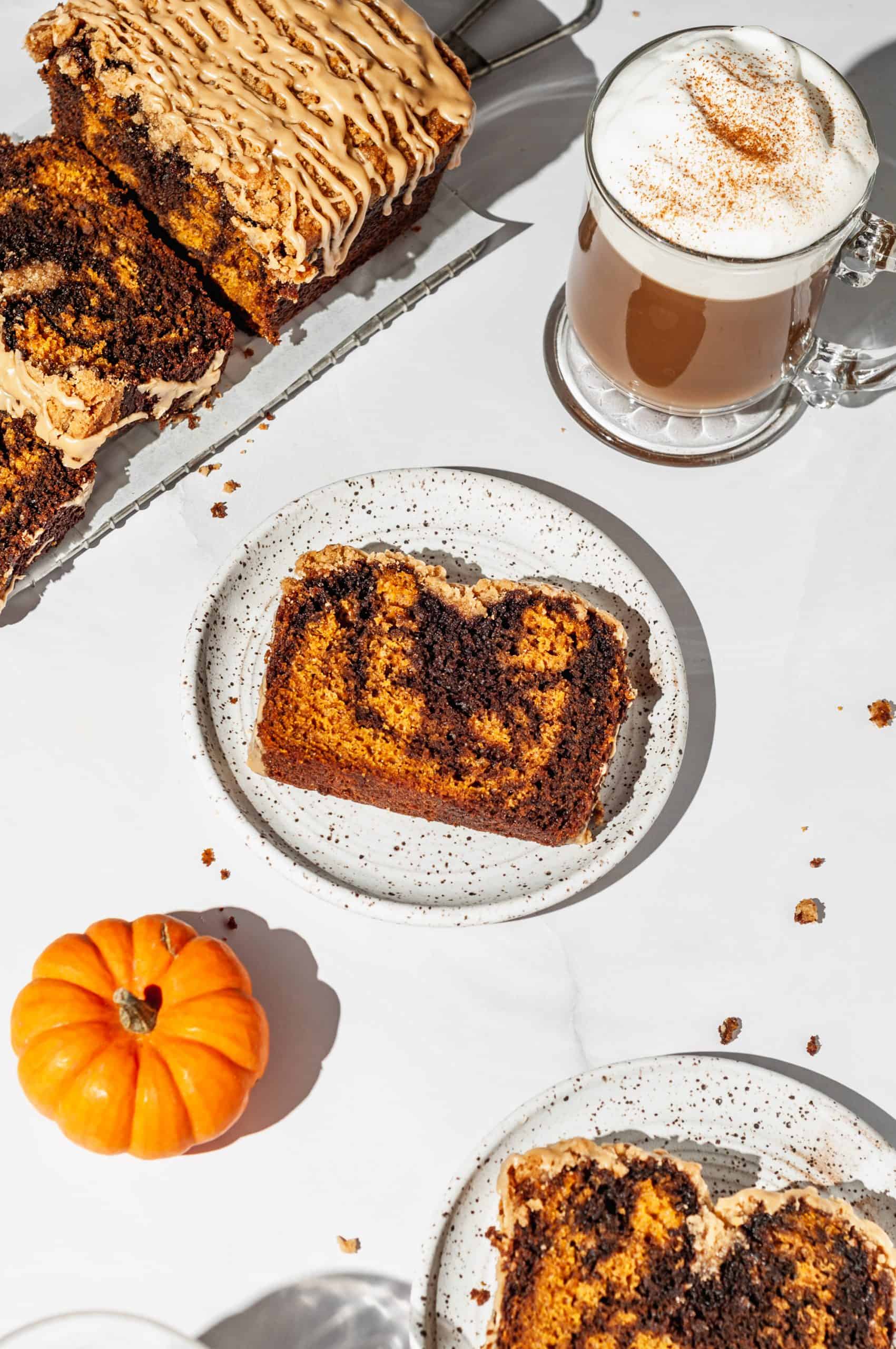 slice of pumpkin spice latte bread on a plate next to mini pumpkins and hot latte