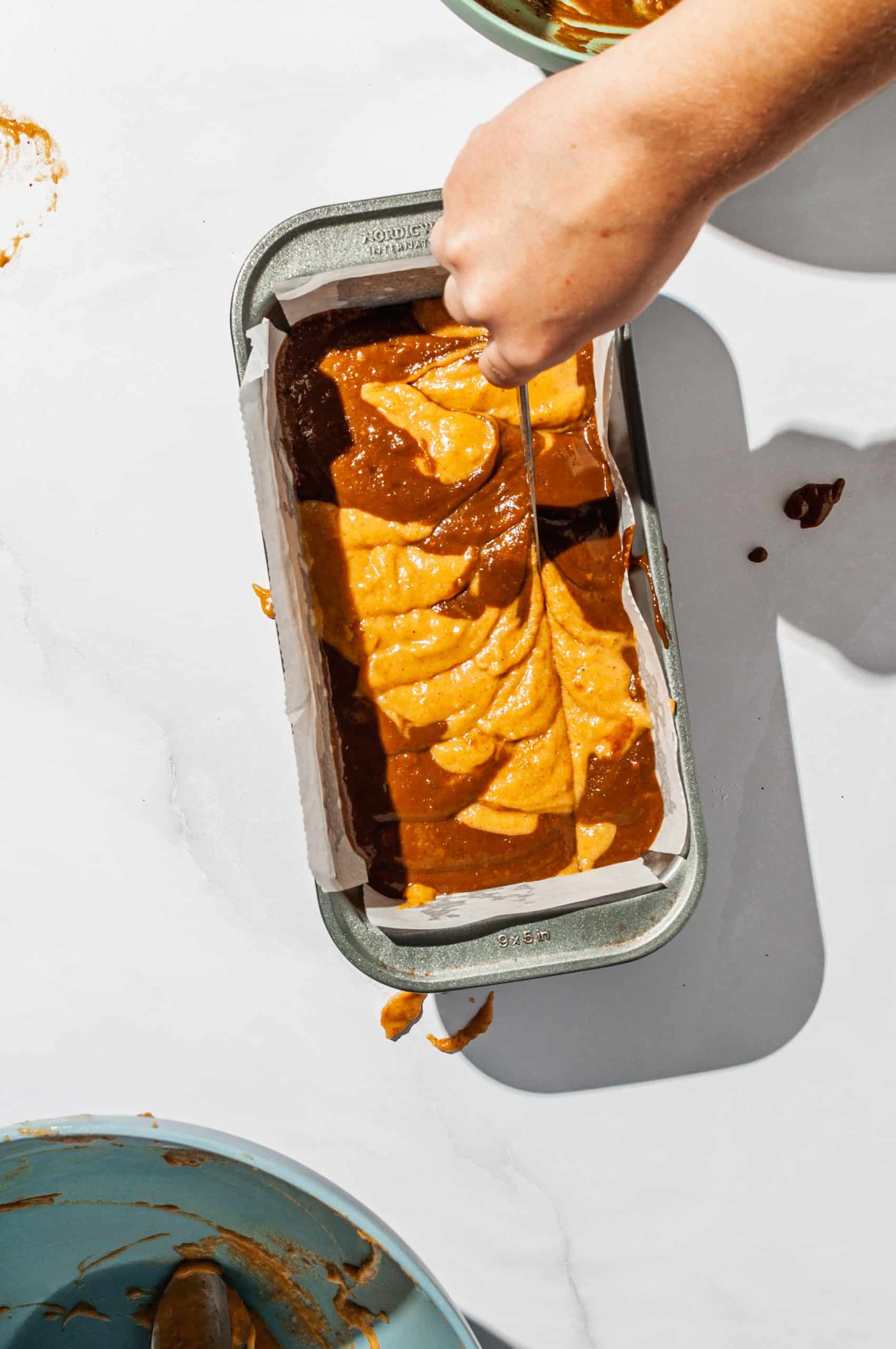 swirling pumpkin and coffee batter in loaf pan with a knife to marble