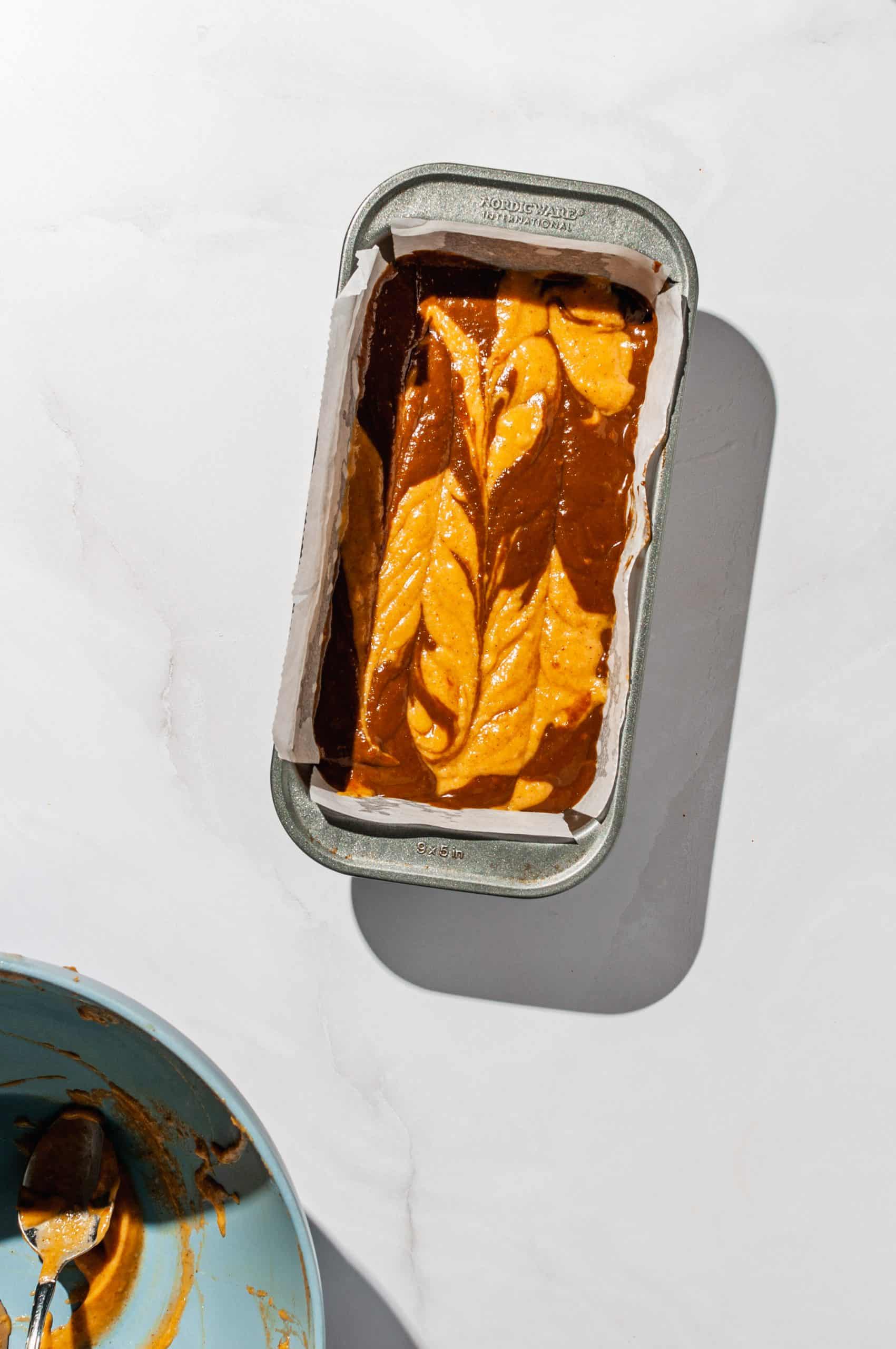 pumpkin and coffee batter in loaf pan swirled with knife before baking