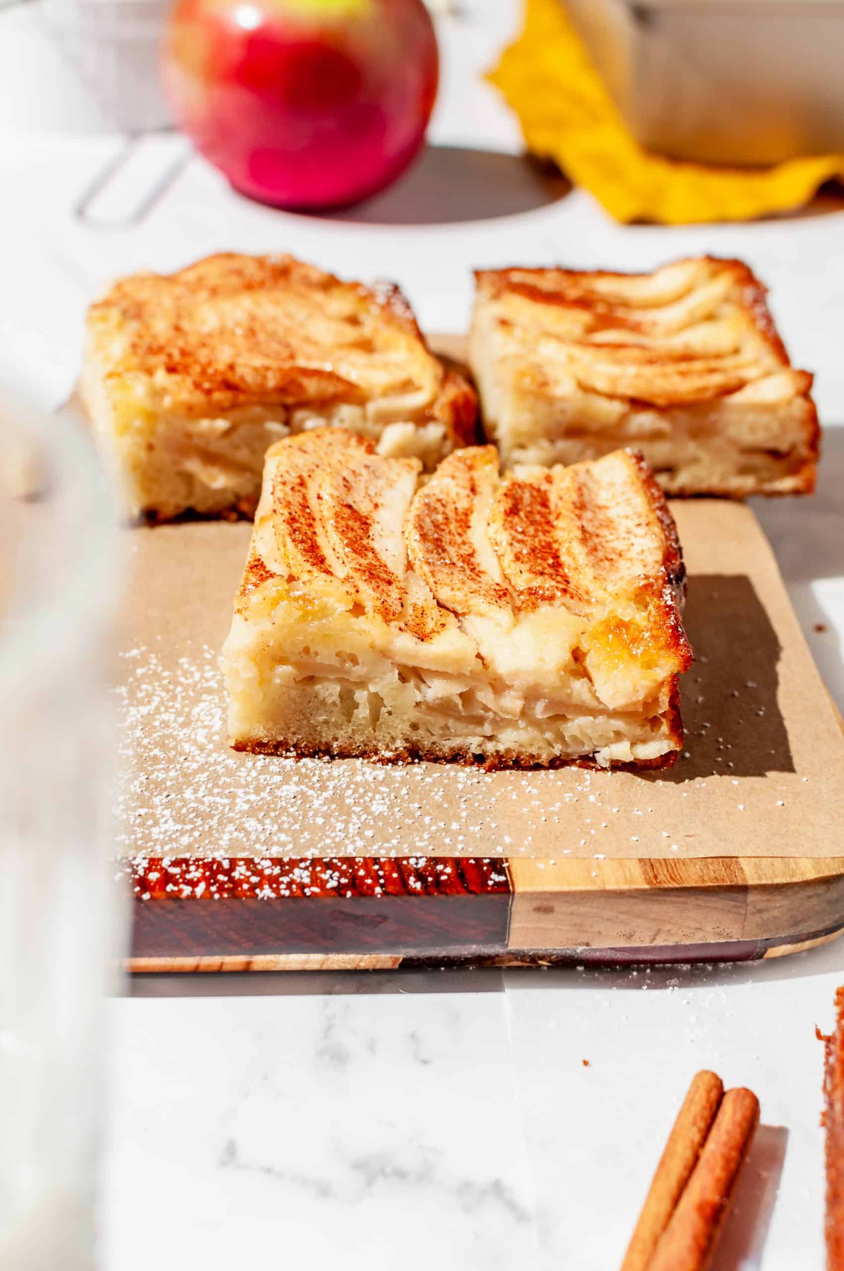 3 pieces of apple snack cake on a small cutting board showing layers of apples inside