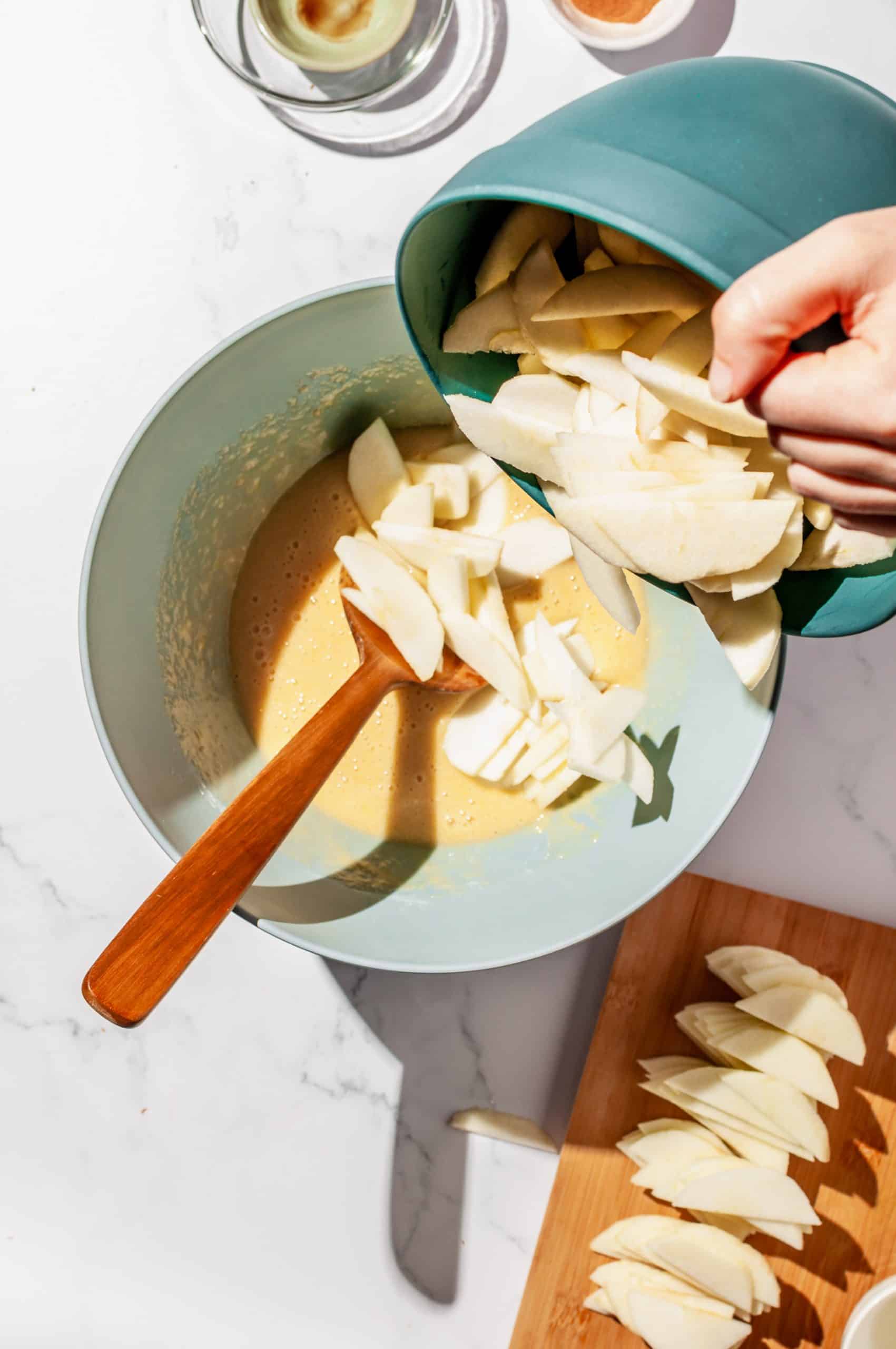 pouring sliced apples from bowl into large bowl with snack cake batter