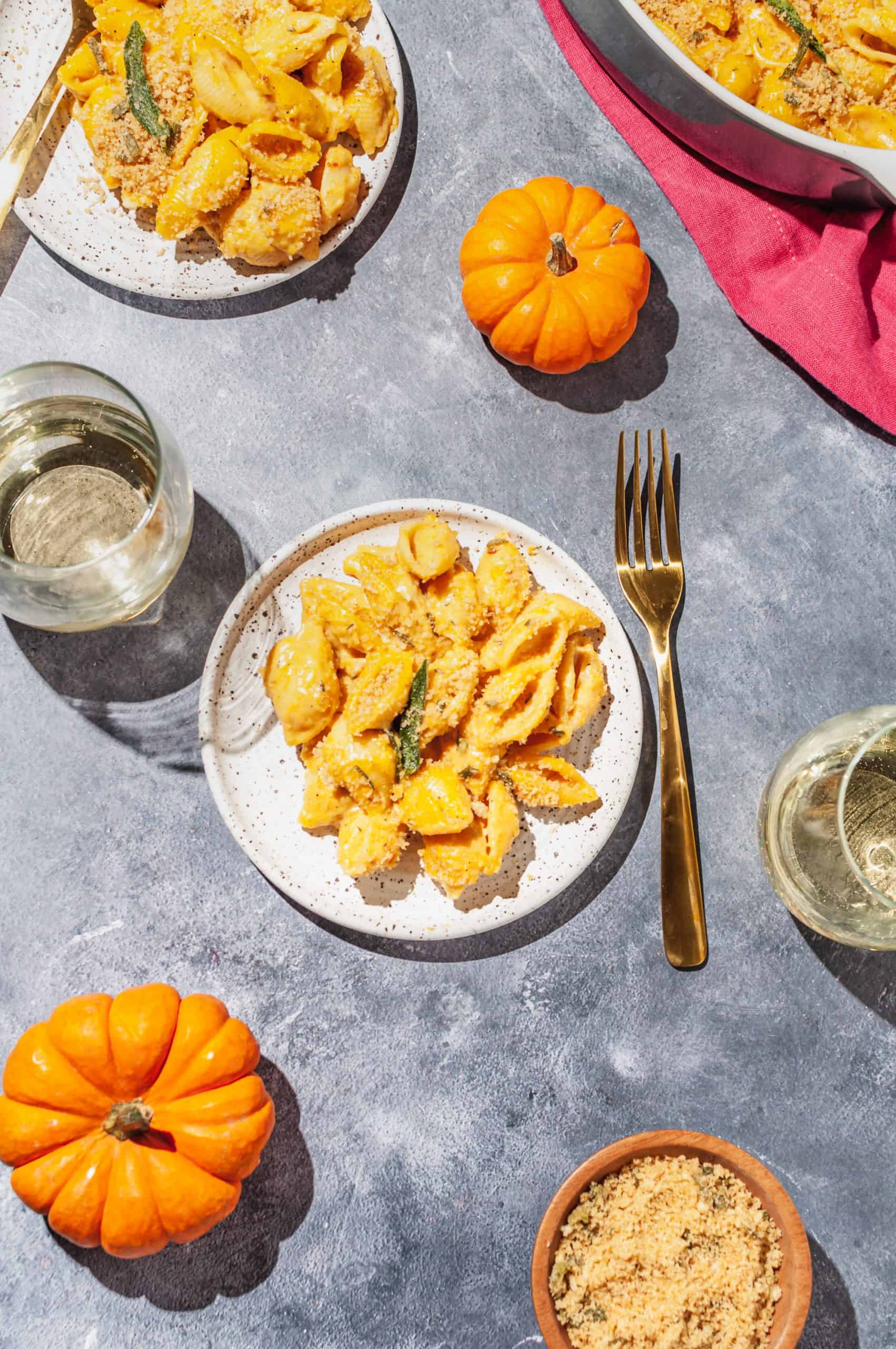 pumpkin mac and cheese on a plate with sage leaf garnish, mini pumpkins to the side