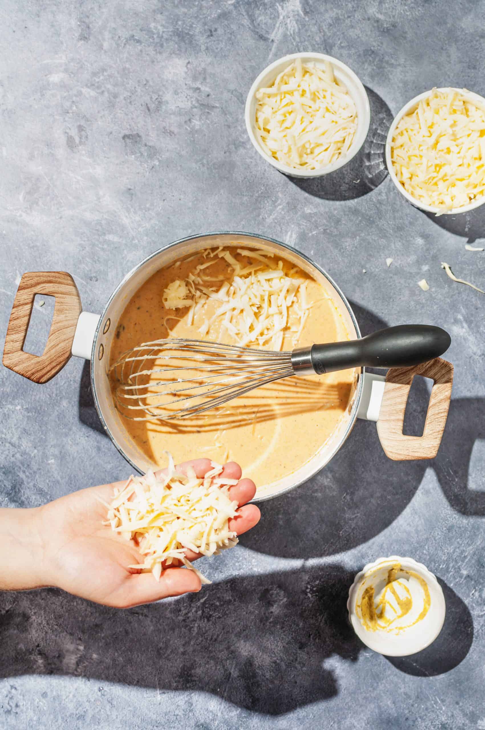 adding handful of shredded cheese to pot of pumpkin mac and cheese sauce