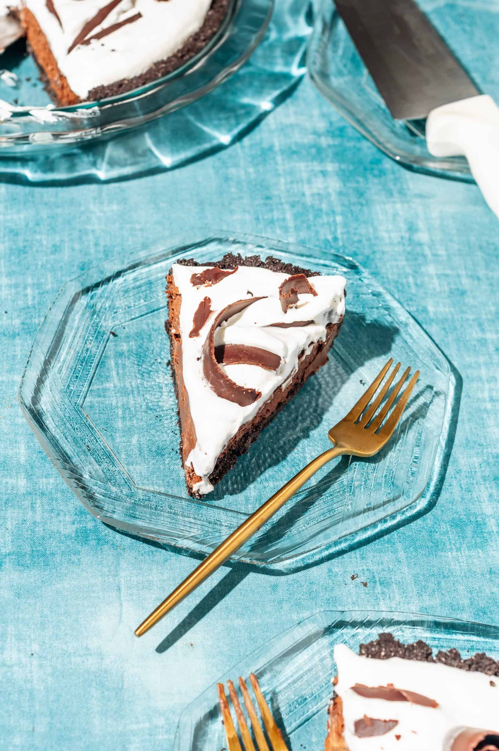 a slice of chocolate satin pie with whipped cream on a plate with a gold fork