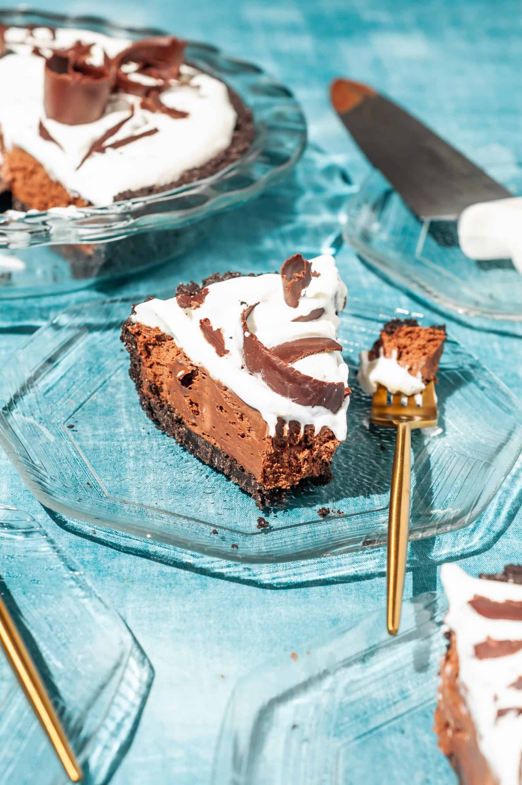 a slice of chocolate satin pie with whipped cream on a glass plate with a gold fork