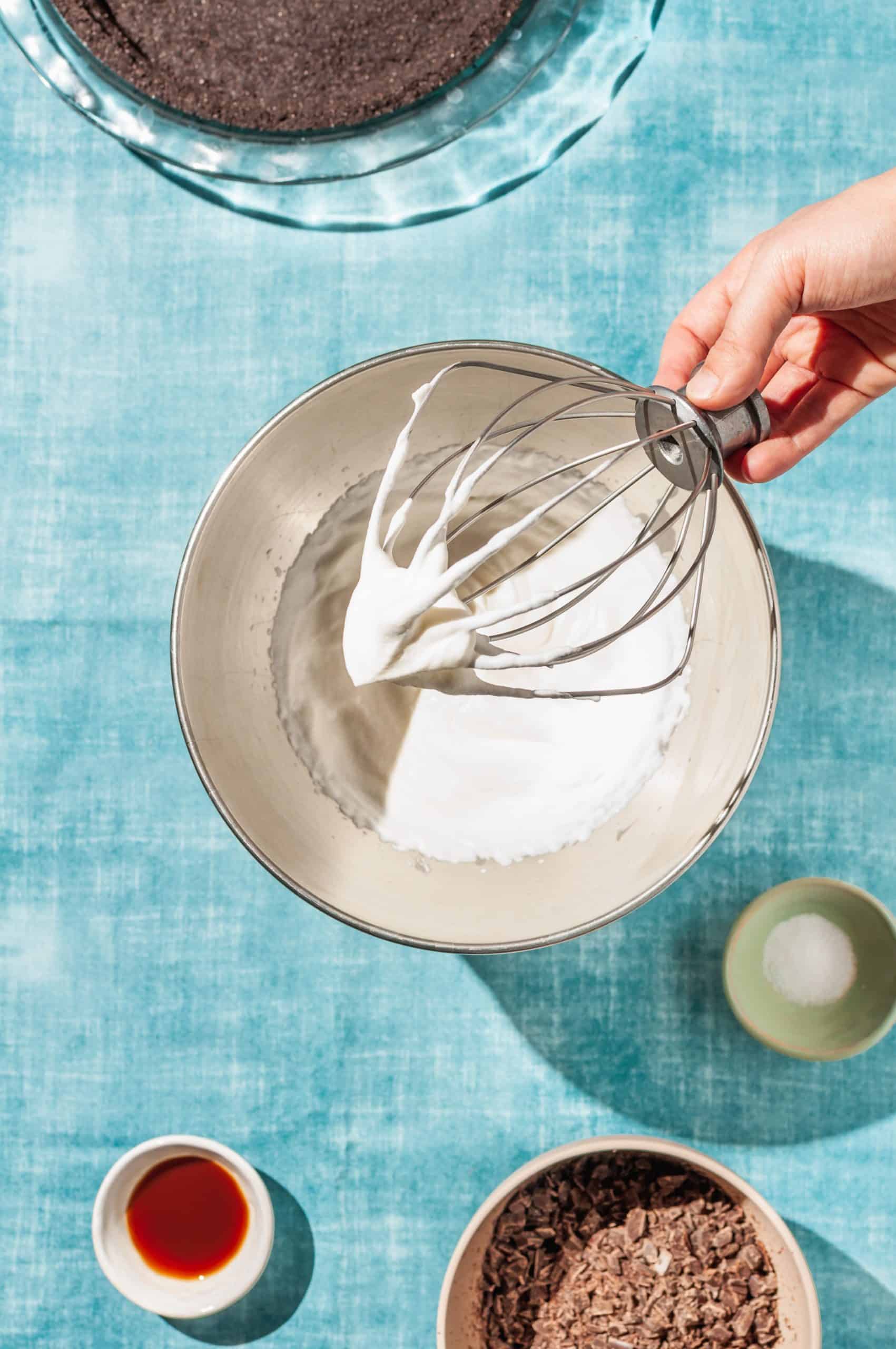 hand holding whisk attachment over a bowl of fresh whipped cream