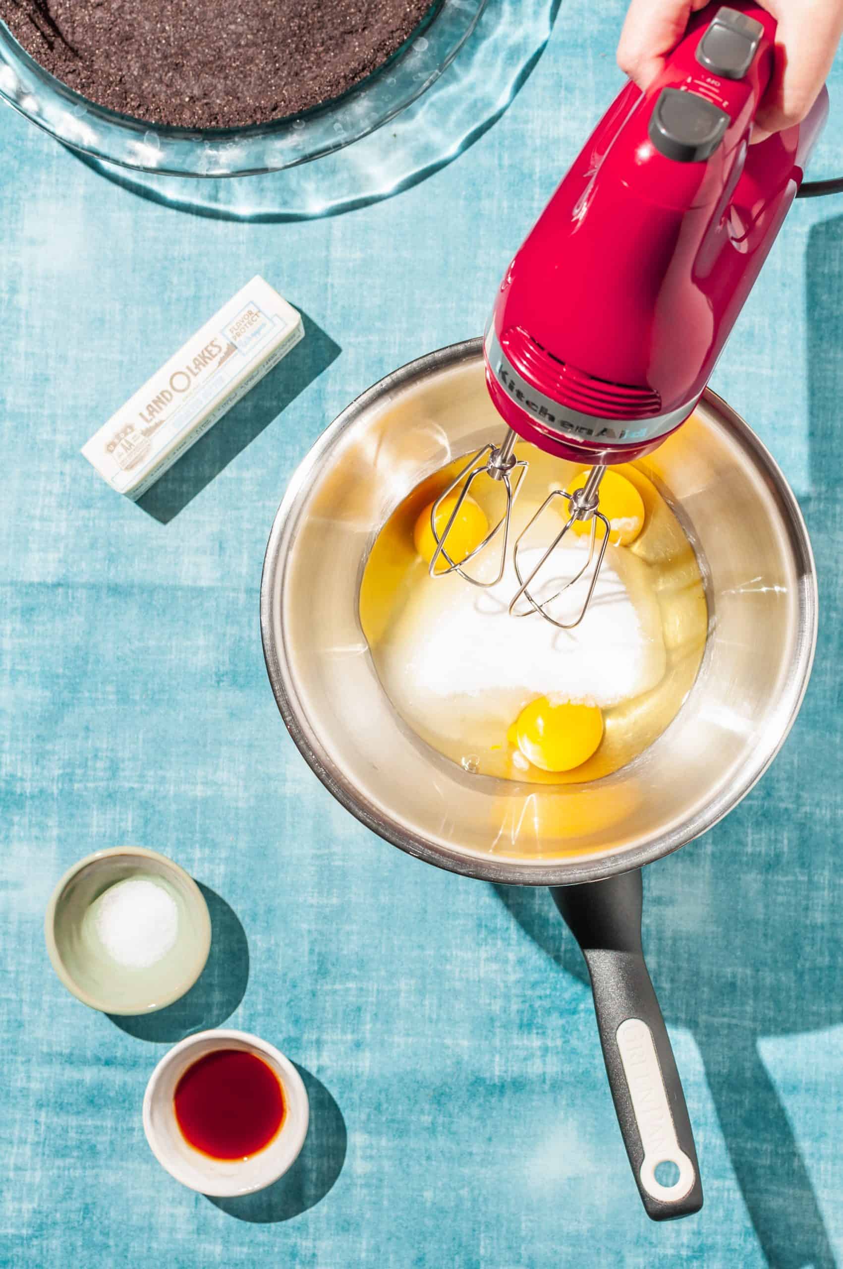 hand holding electric beater in bowl with eggs and sugar set over double broiler