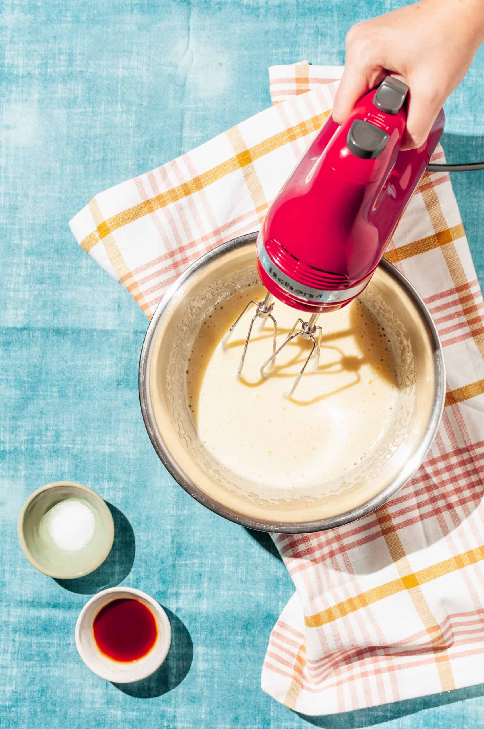 hand holding electric beater in bowl of egg custard