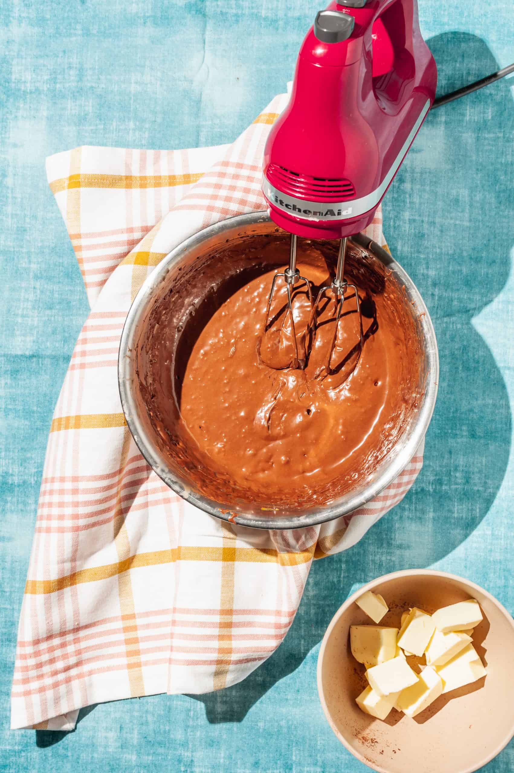 bowl of creamy chocolate mousse mixture with electric beater, cubed butter to the side