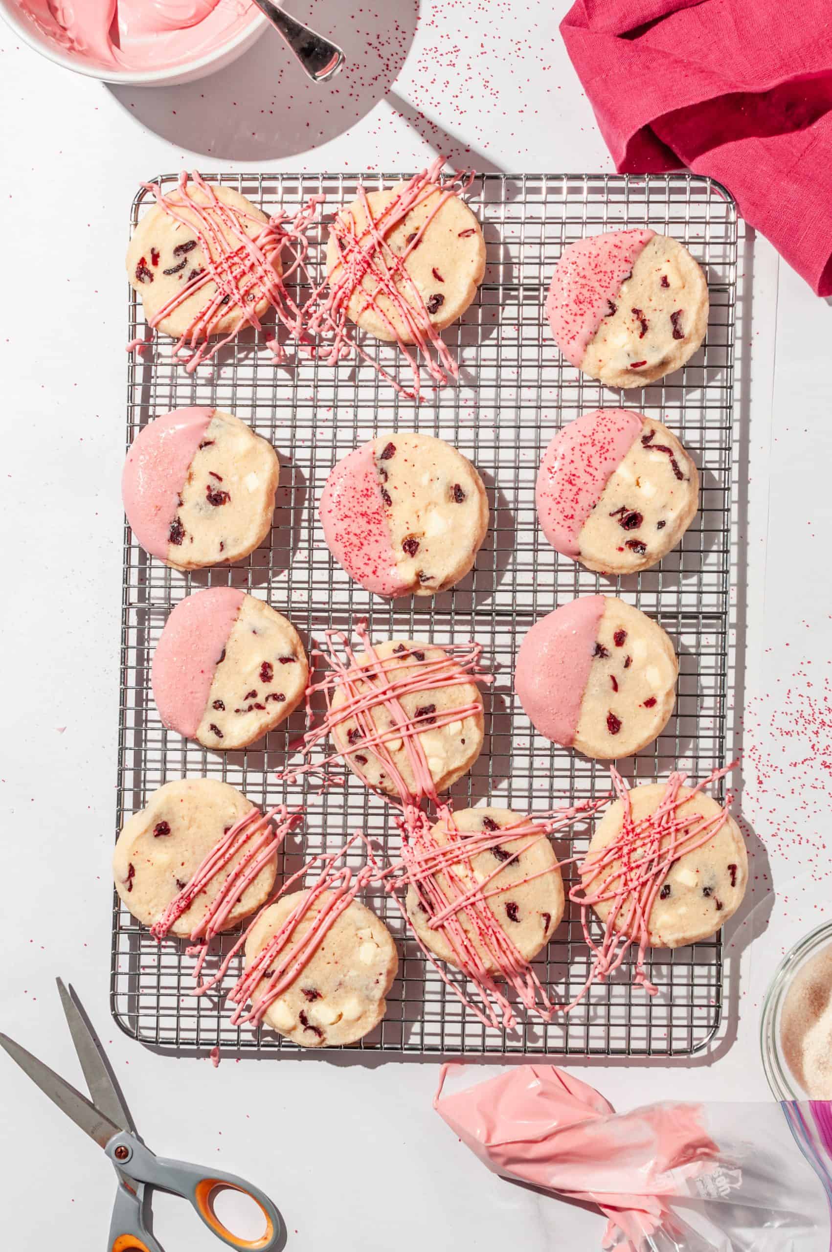 cranberry shortbread cookies on a wire rack after being drizzled with melted pink white chocolate