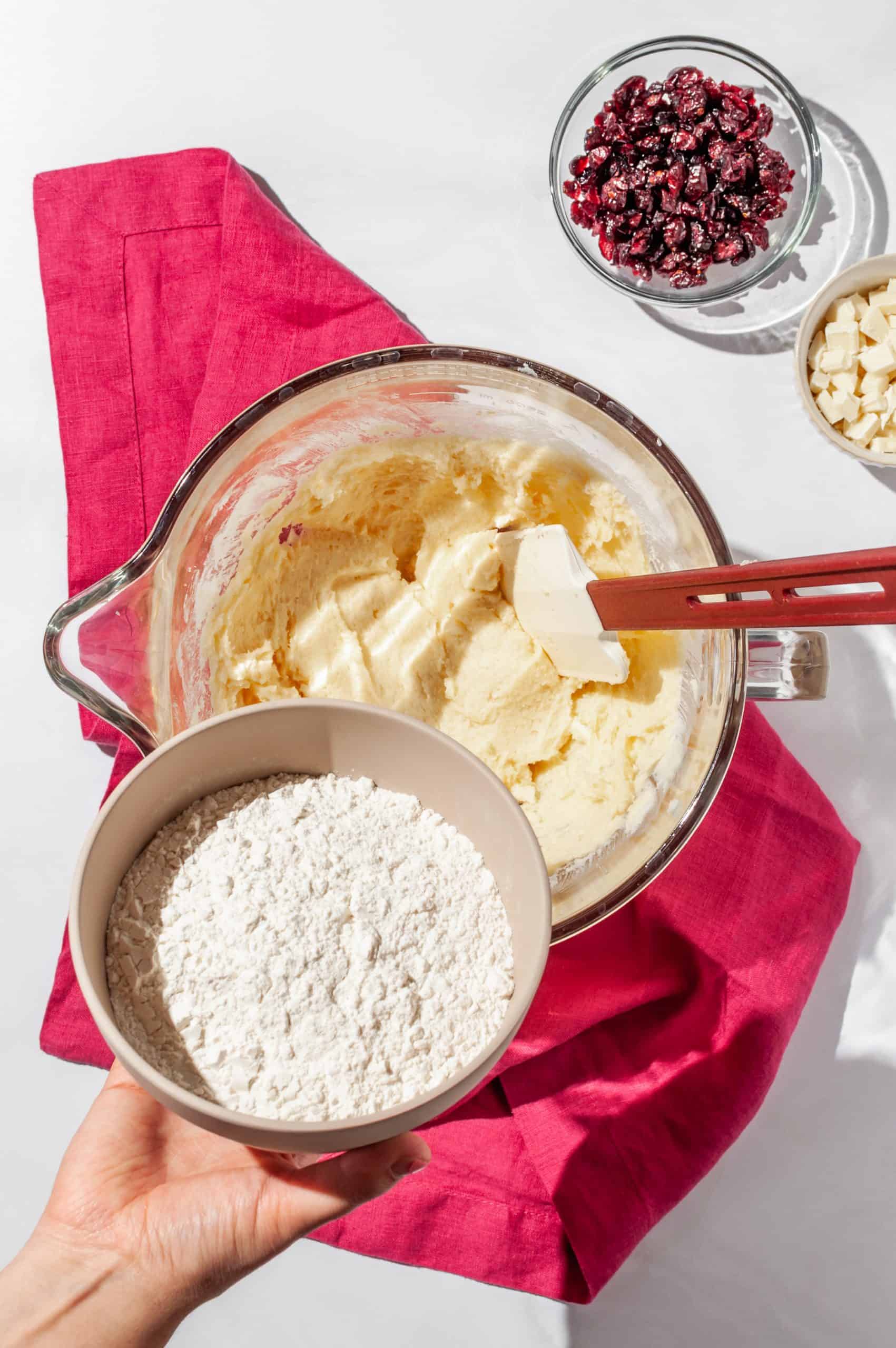 adding flour to mixing bowl to complete base shortbread dough, cranberry and white chocolate to the side