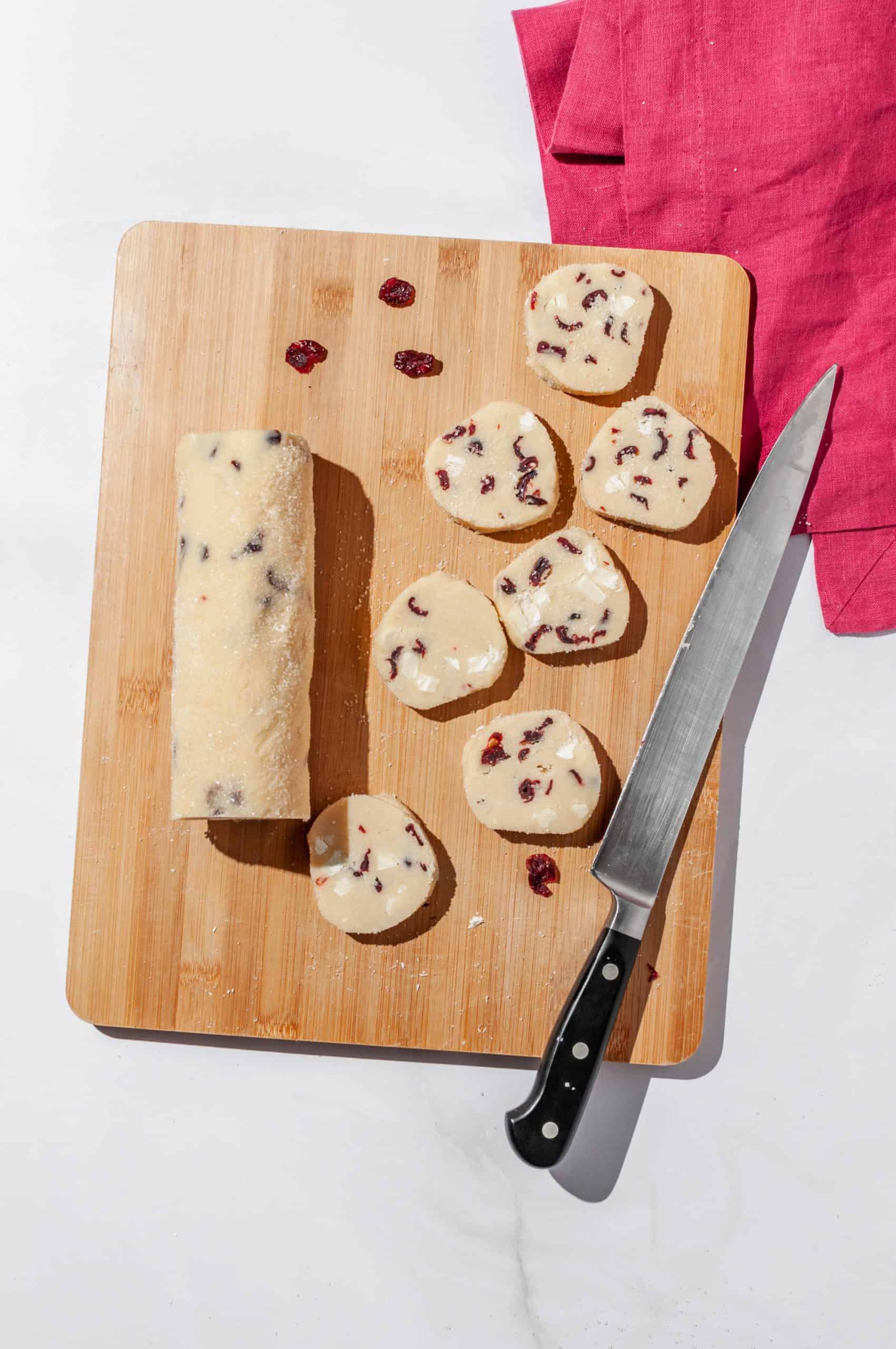 log of cranberry white chocolate shortbread dough sliced into 7 rounds on a cutting board