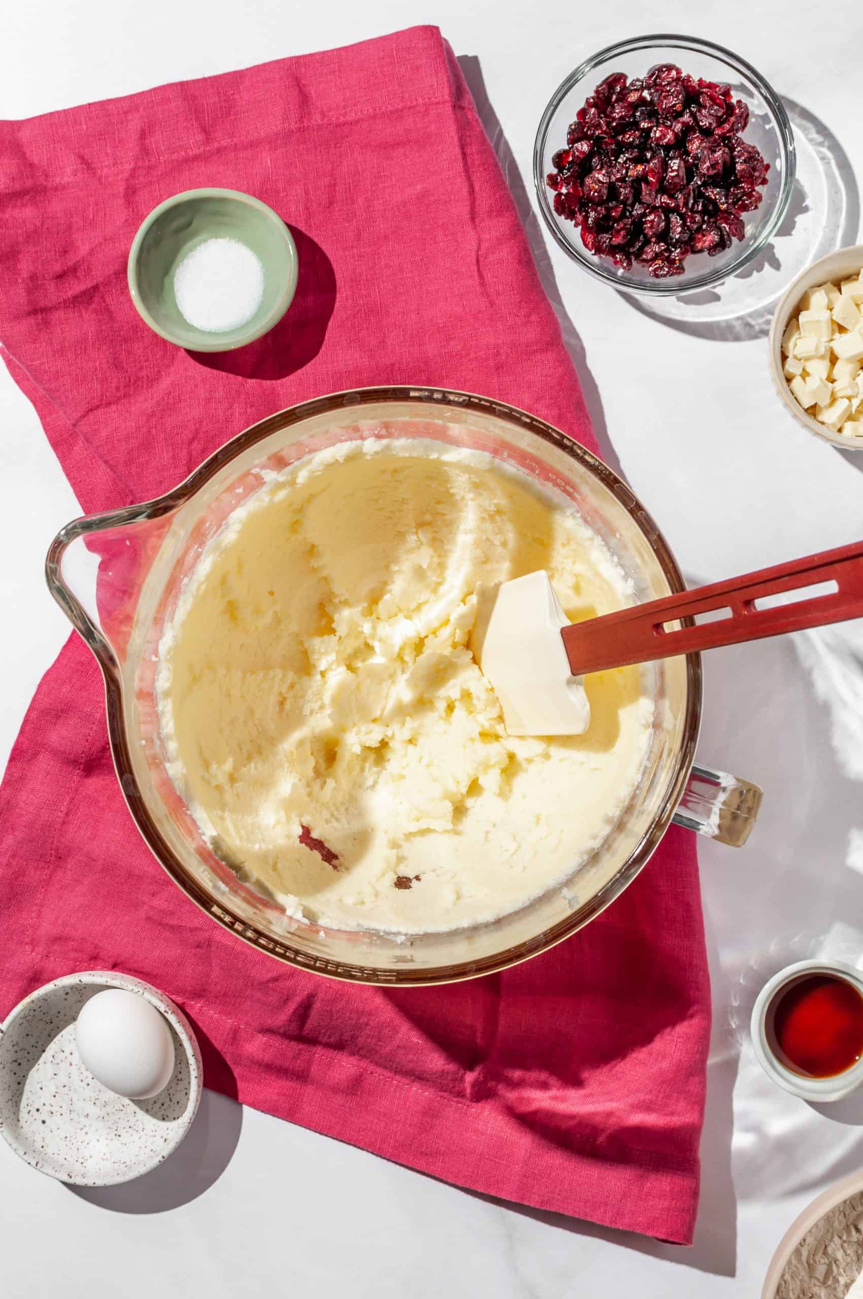 butter and sugar creamed together in a mixing bowl, dried cranberries and other shortbread ingredients on the side