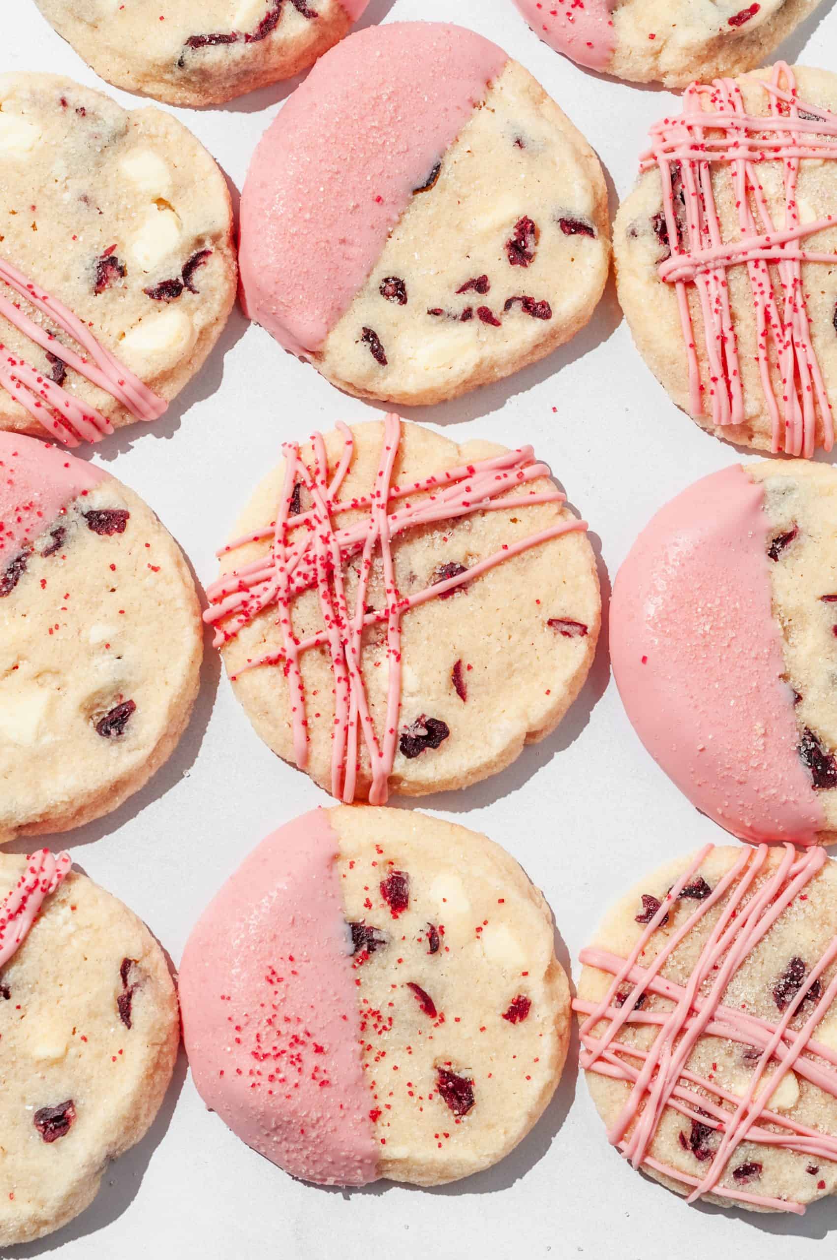 overhead close up of cranberry shortbread cookies decorated with pink white chocolate patterns and sanding sugar