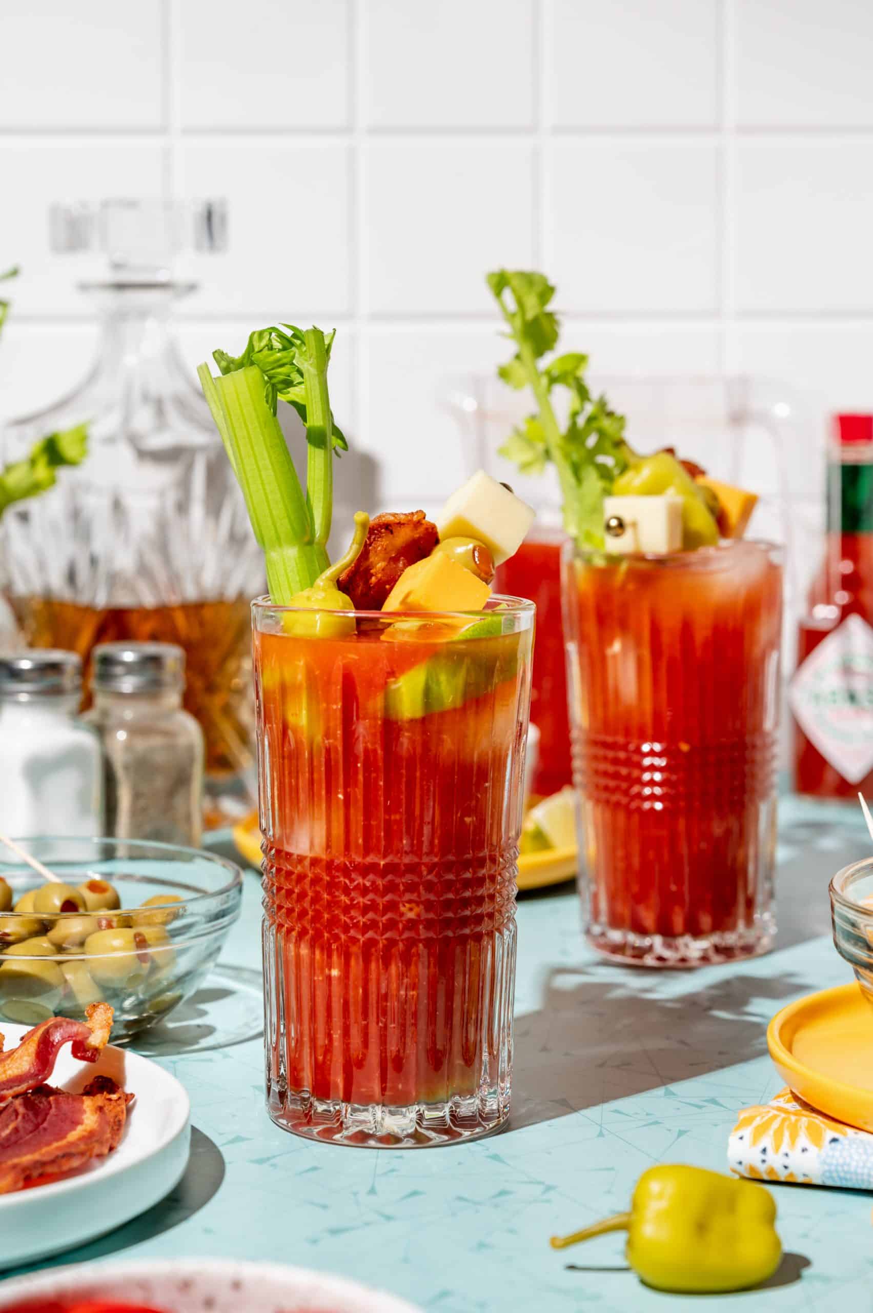 Two bloody mary cocktails with bacon, celery, and other garnishes