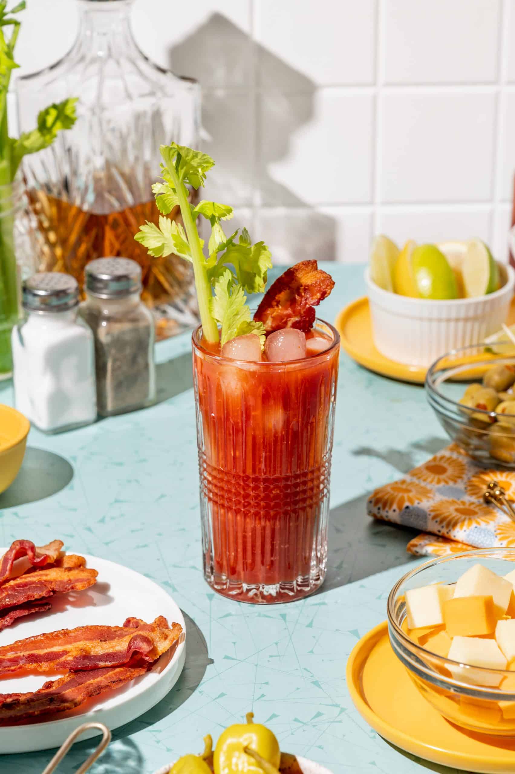 A bloody mary cocktail in a glass with a strip of bacon and a celery stalk.