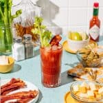 A bloody mary cocktail in a glass with a strip of bacon and a celery stalk