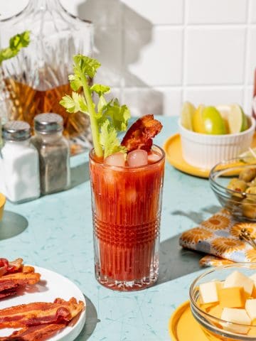A bloody mary cocktail in a glass with a strip of bacon and a celery stalk