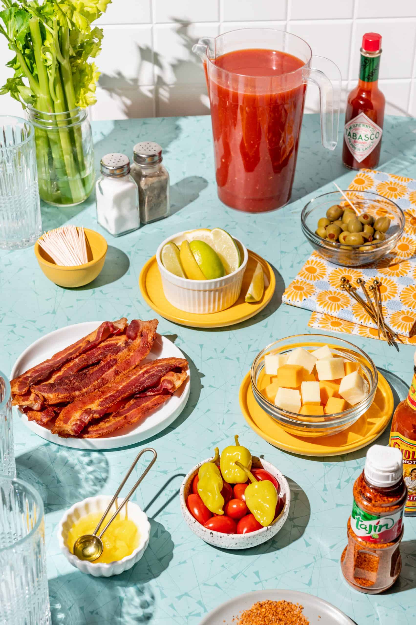 fixins for a DIY bloody mary bar: celery, lemon and lime wedges, cheese cubes, bacon, peppers, hot sauce